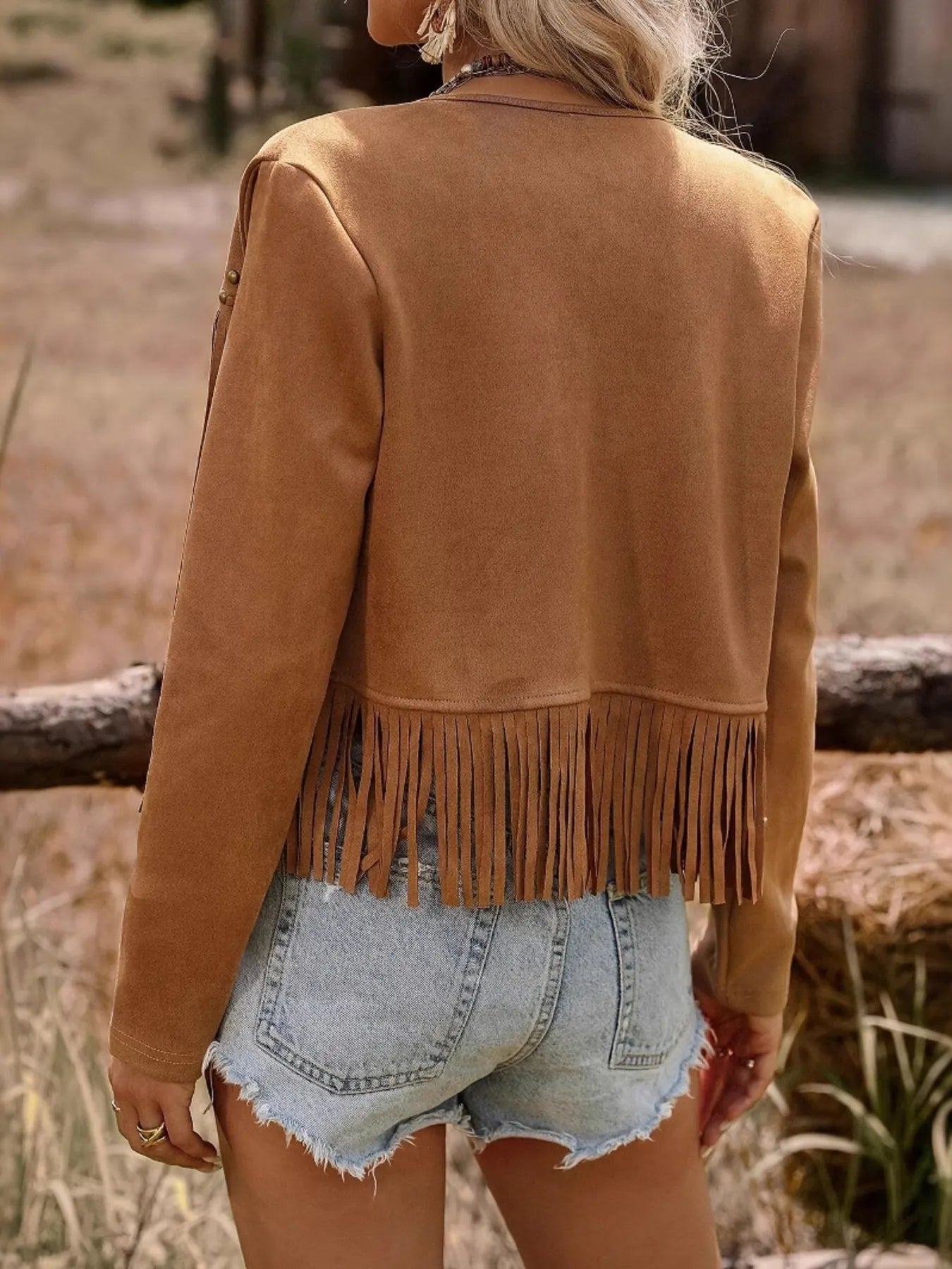 Back view of the model wearing the Trendy Fringe Studded Open Front Jacket, showcasing the fringe detail and overall stylish design, paired with denim shorts.