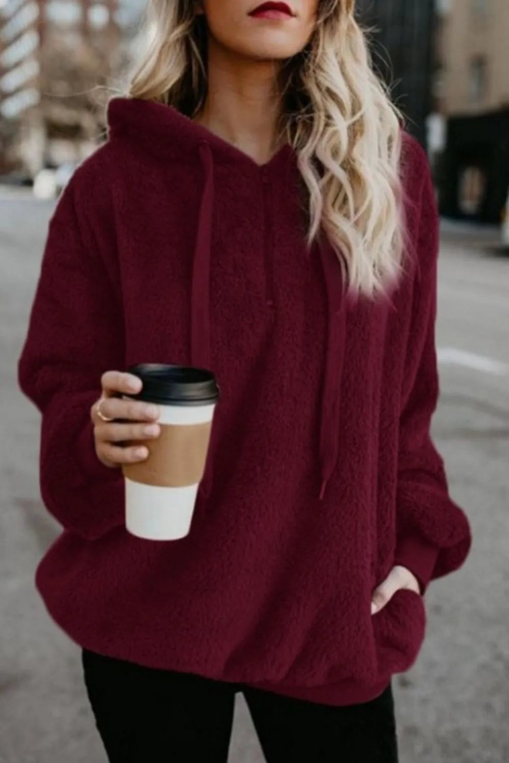 Model wearing a Cozy Full Size Teddy Hoodie with Quarter-Zip and Drawstring in burgundy, holding a coffee cup outdoors.