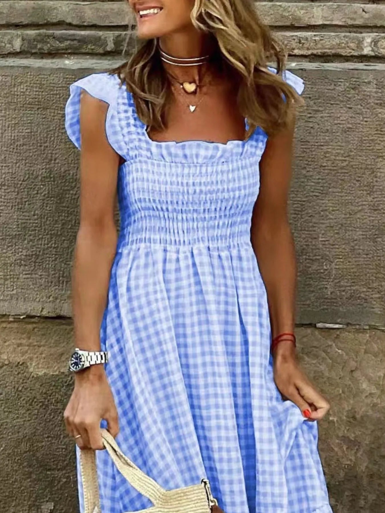 Stylish woman wearing a Gingham Maxi Dress with Ruffle Straps, Smocked Bodice & Tiered Design, featuring a blue and white checkered pattern, smiling outdoors.