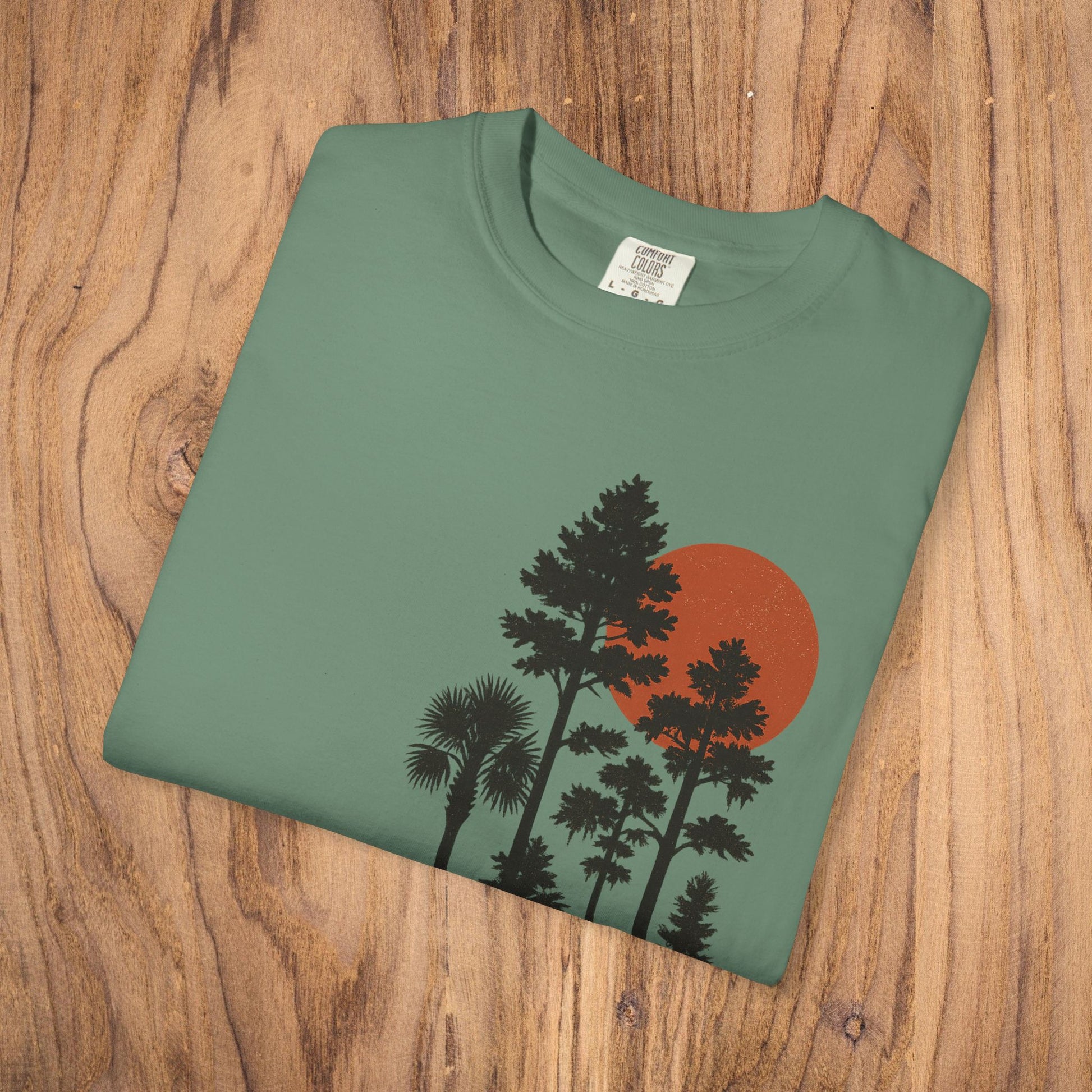 Sunset Trees Unisex T-Shirt folded on wooden surface, made of soft 100% cotton, perfect for casual wear.