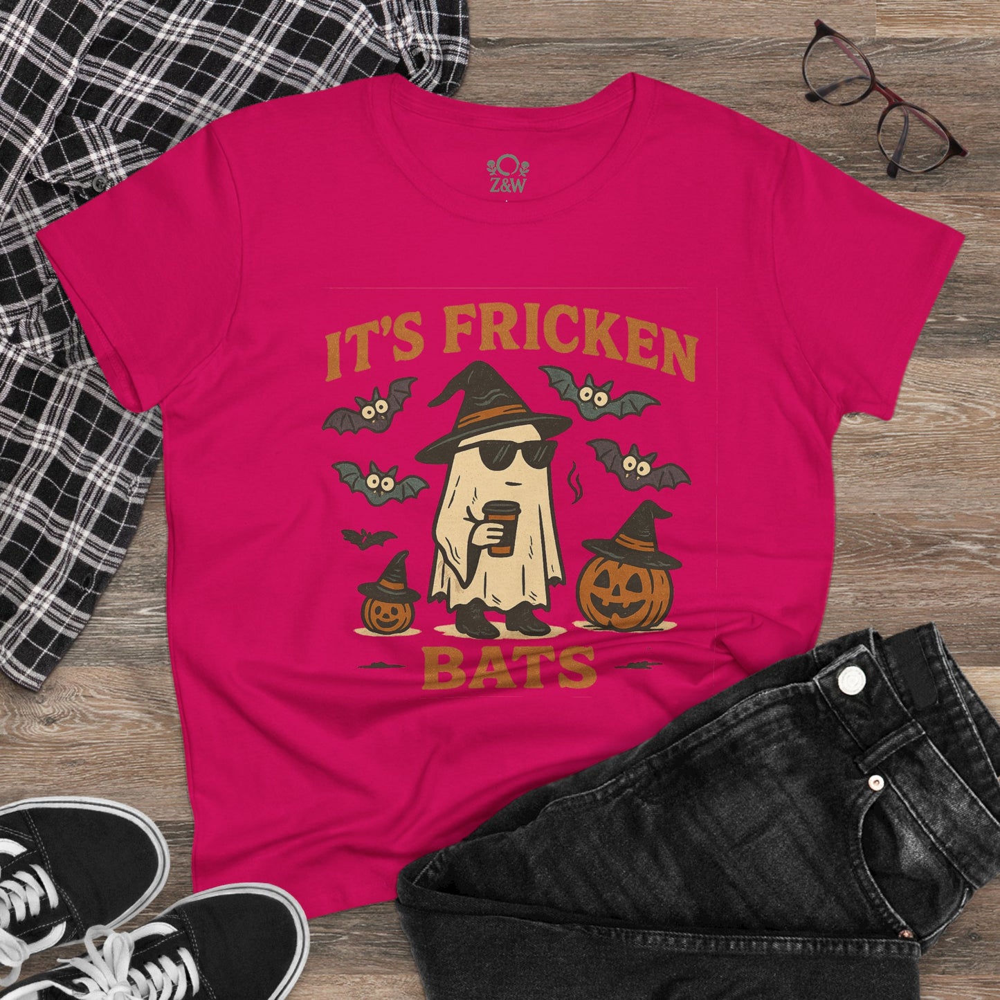 Stylish flat lay of a pink Halloween unisex t-shirt with the graphic 'It's Fricken Bats,' paired with denim shorts and sneakers, perfect for a fun night out or trick-or-treating.