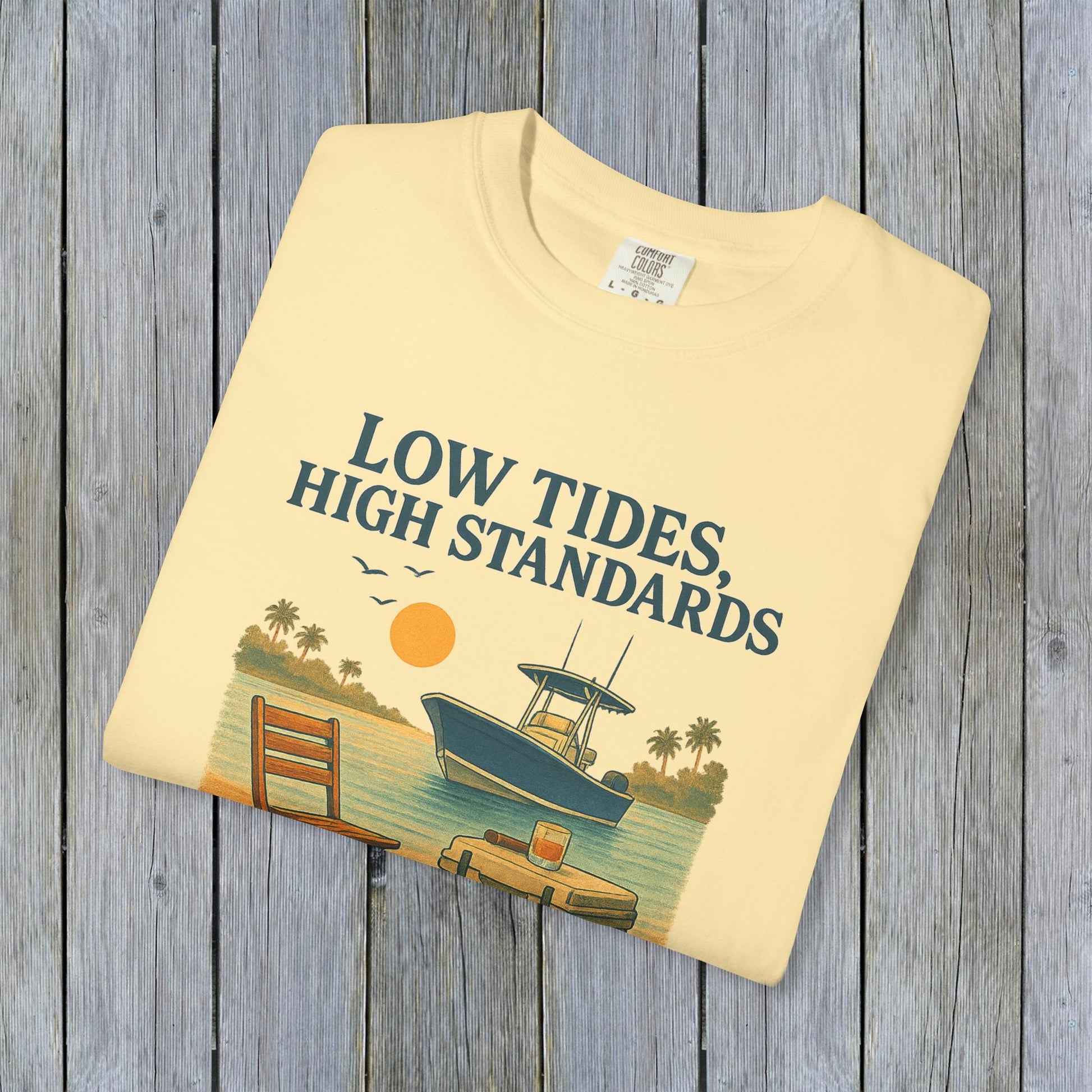 Garment-Dyed Low Tides High Standards T-Shirt folded on a textured wooden background, highlighting its soft fabric and colorful beach-themed graphic.