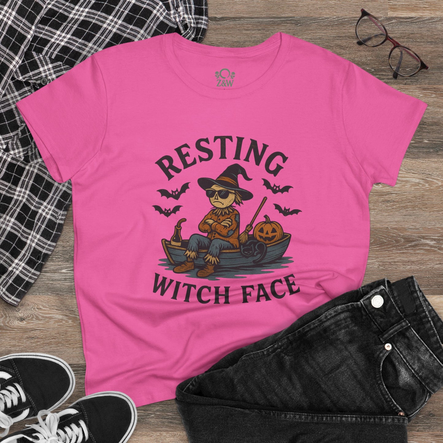 Resting Witch Face Halloween T-Shirt for Women on a flat lay with jeans and glasses. The pink tee features a creative design of a witch, making it a great choice for party attire or gifts.