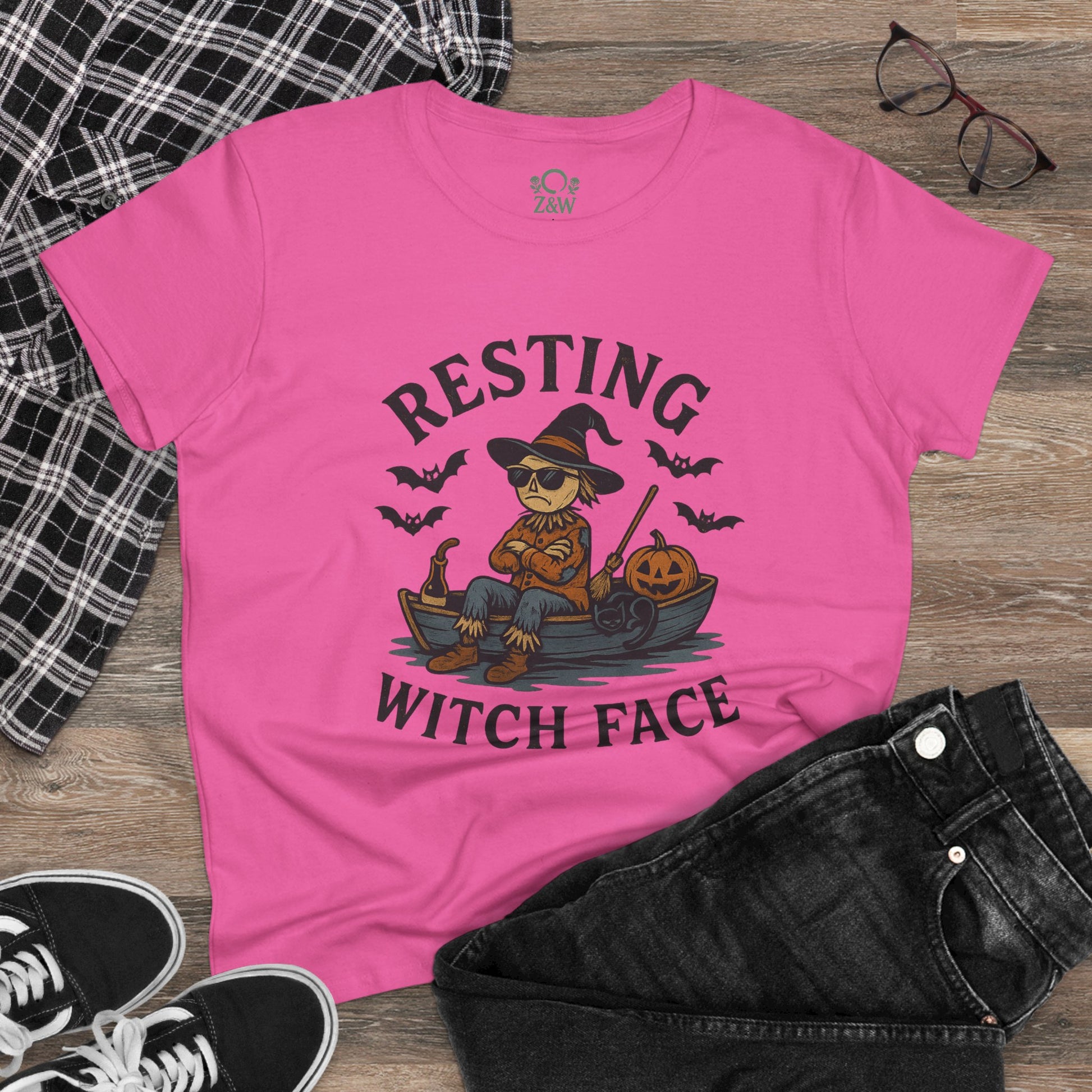 Resting Witch Face Halloween T-Shirt for Women on a flat lay with jeans and glasses. The pink tee features a creative design of a witch, making it a great choice for party attire or gifts.