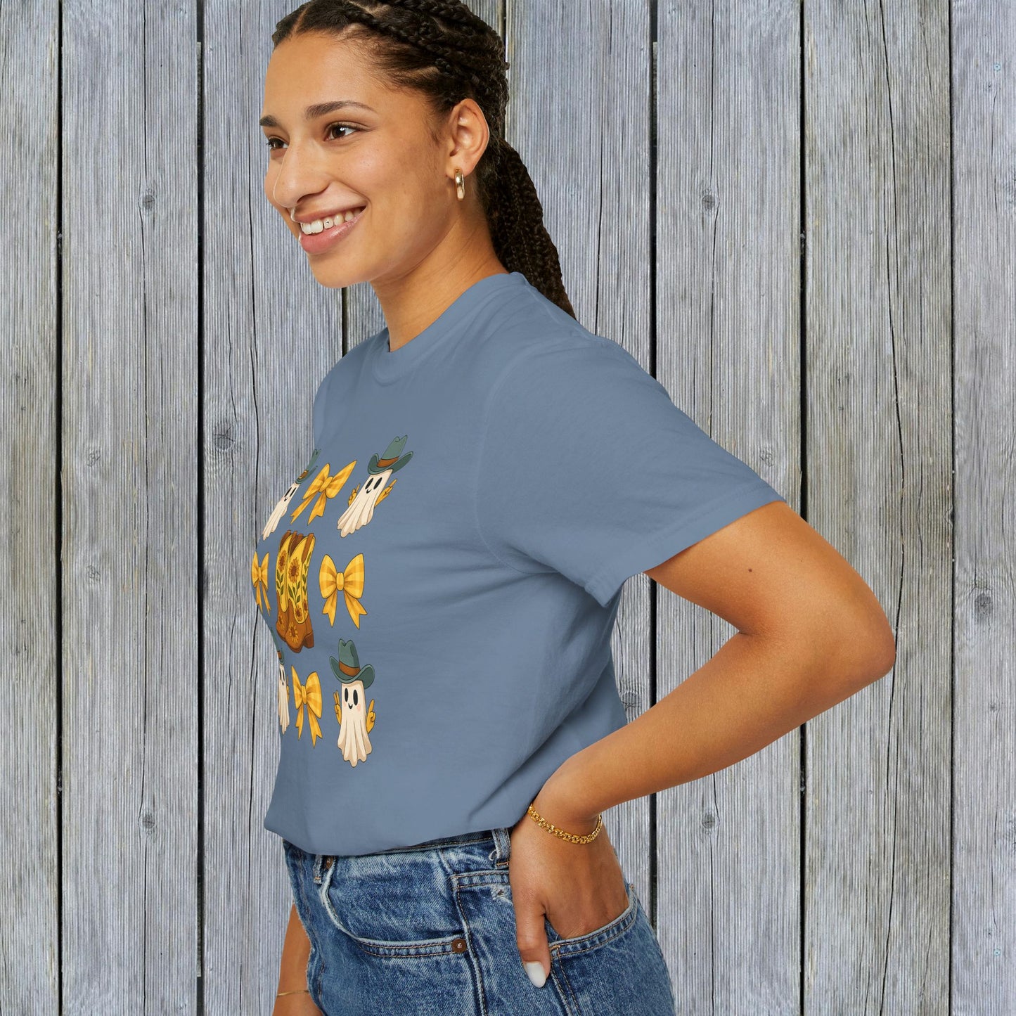 Cute Halloween T-Shirt featuring ghosts and cowboy boots, modeled by a woman in a blue shirt against a rustic wooden background. Perfect for unisex fall fashion with eco-friendly fabric.