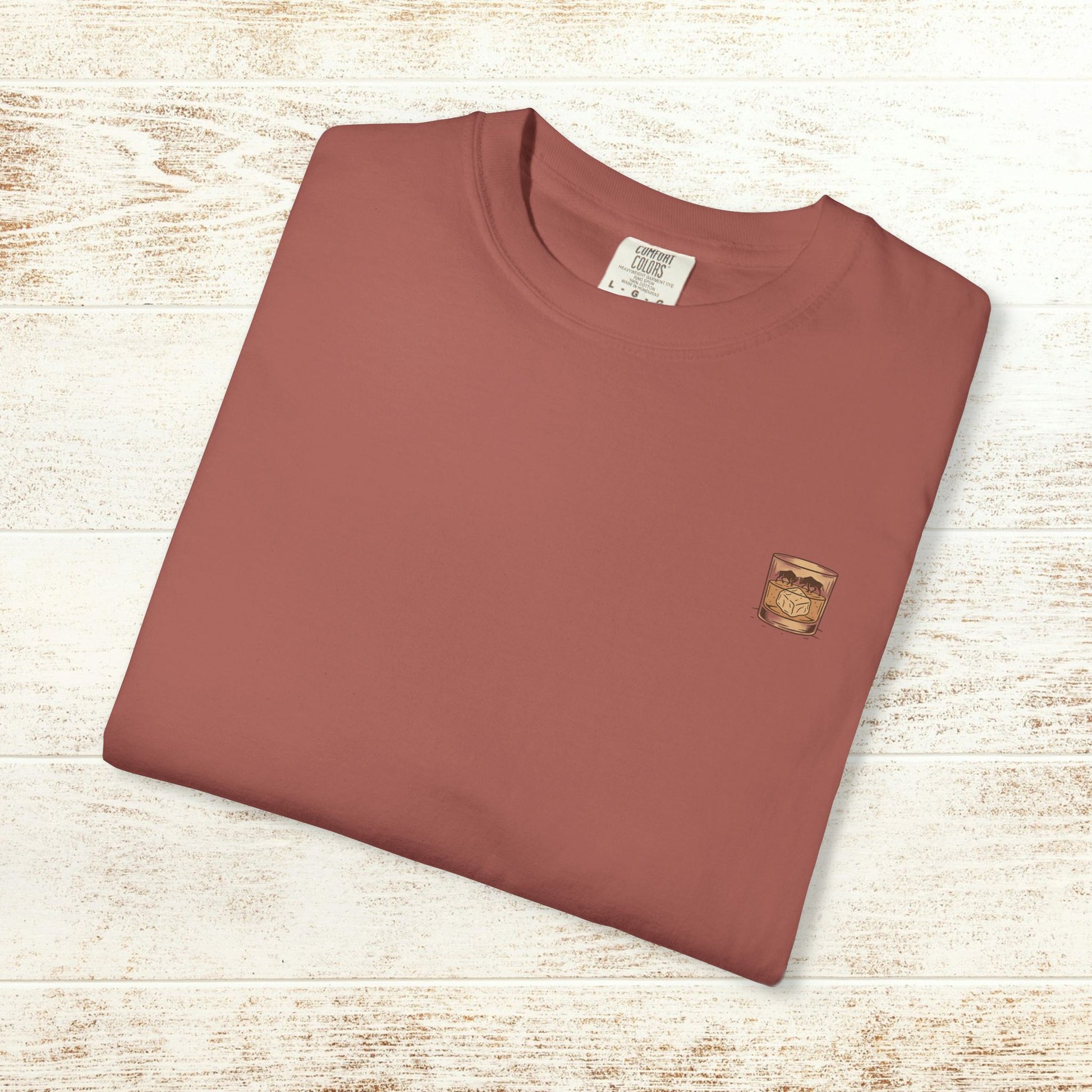 Folded Rodeo On The Rocks Tee in a warm hue, with a logo of a drink glass, emphasizing its soft, durable fabric and unique garment-dyed style.