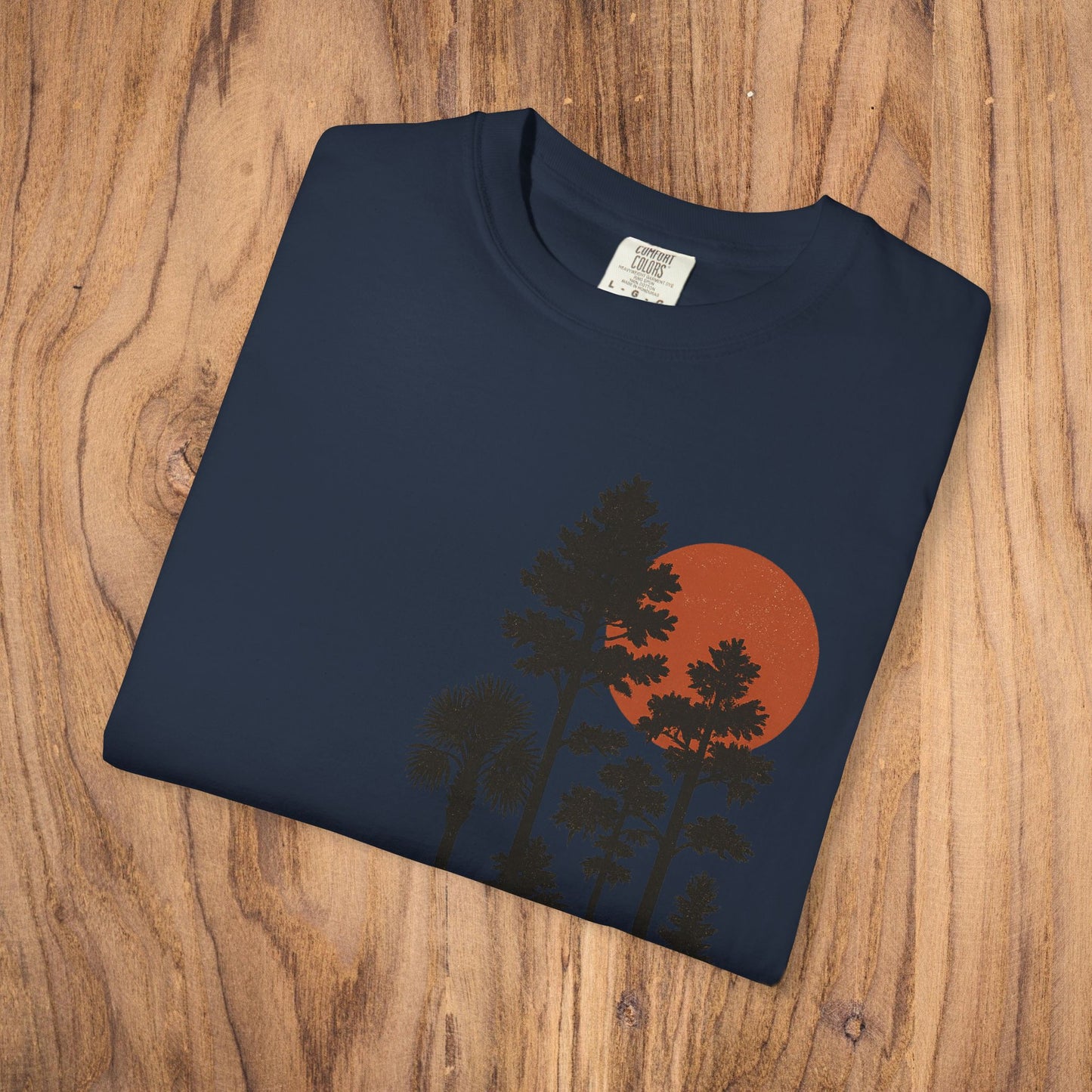 Folded Sunset Trees Unisex T-Shirt displaying the unique graphic design of trees against a sunset, made from soft garment-dyed cotton.