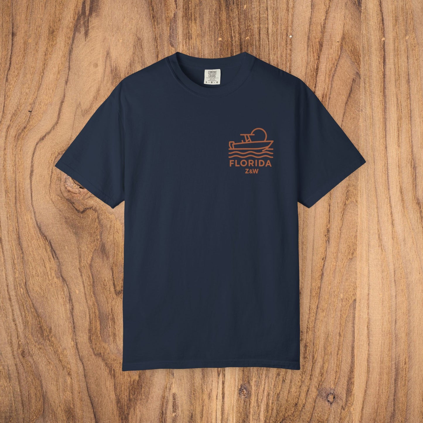 Unisex Florida Graphic Tee displayed on a wooden background, featuring a boat design and soft garment-dyed US cotton material, perfect casual wear.