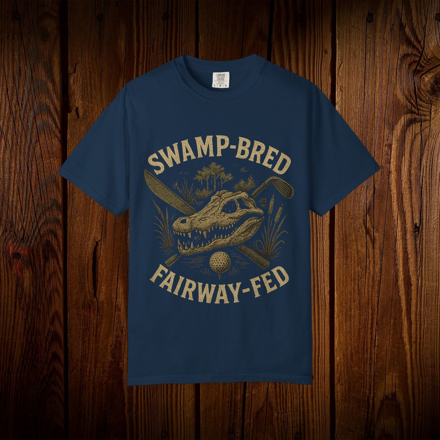 Unisex Swamp-Bred Fairway-Fed Tee in navy blue, displaying an eye-catching design with an alligator skull and golf paraphernalia on a wooden background.