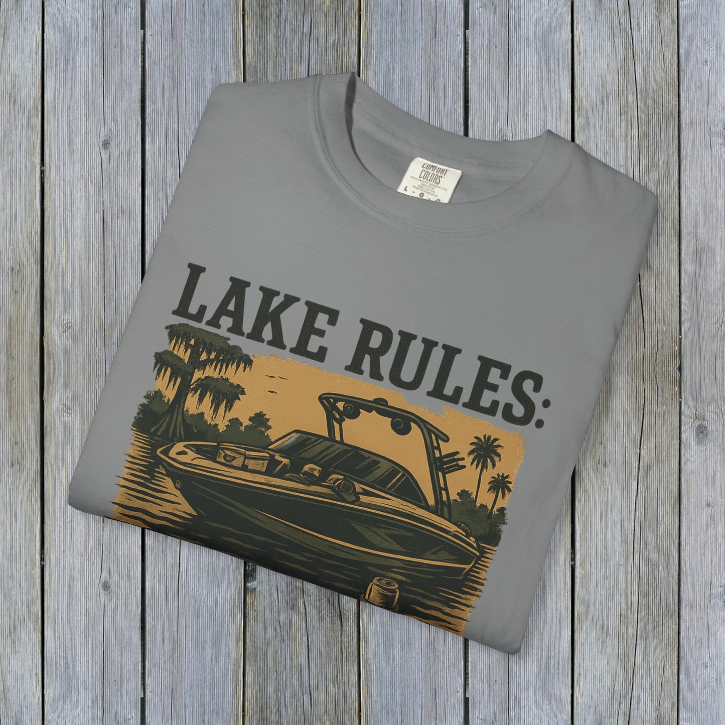Folded Unisex Garment-Dyed Lake Rules Tee displayed on rustic wood, featuring bold lake rules branding ideal for casual outings.