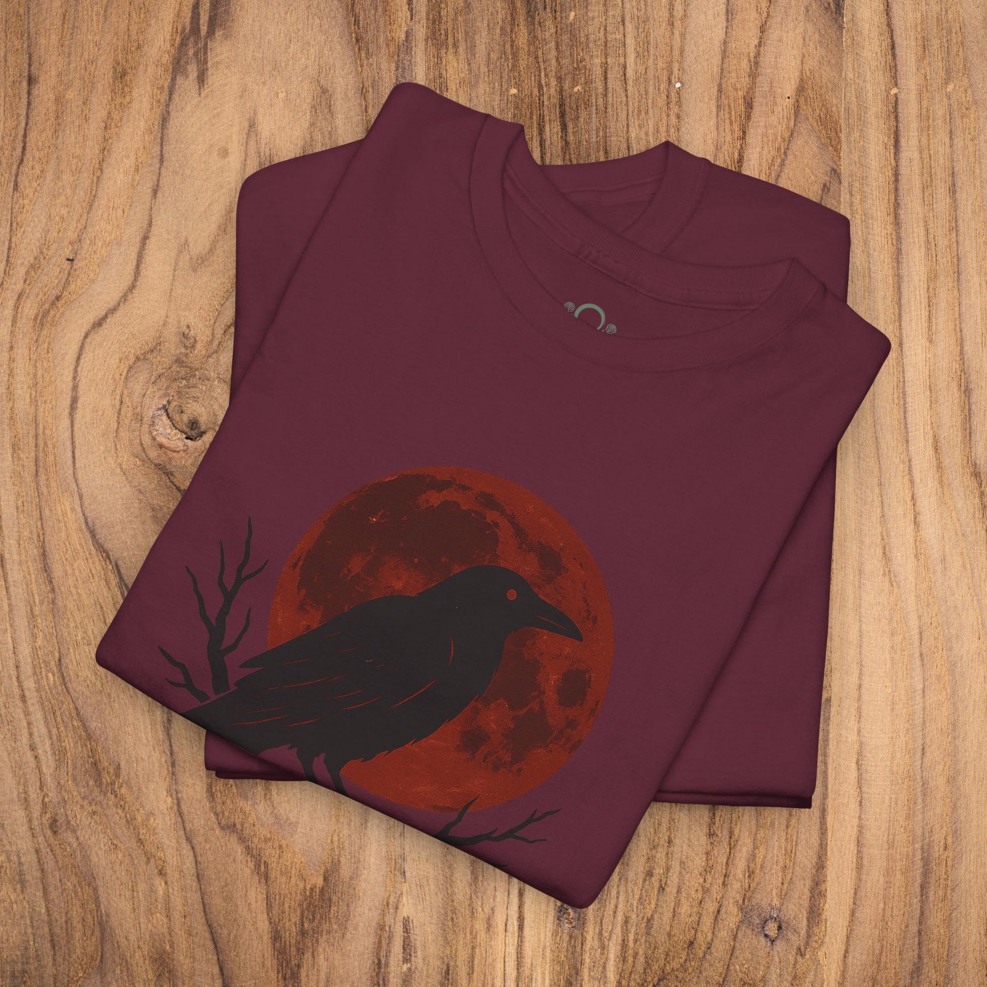 Gothic Raven T-Shirt showcasing a raven silhouette with a red moon backdrop, making it an ideal spooky gift for Halloween. Heavy cotton material and perfect for casual fall fashion.