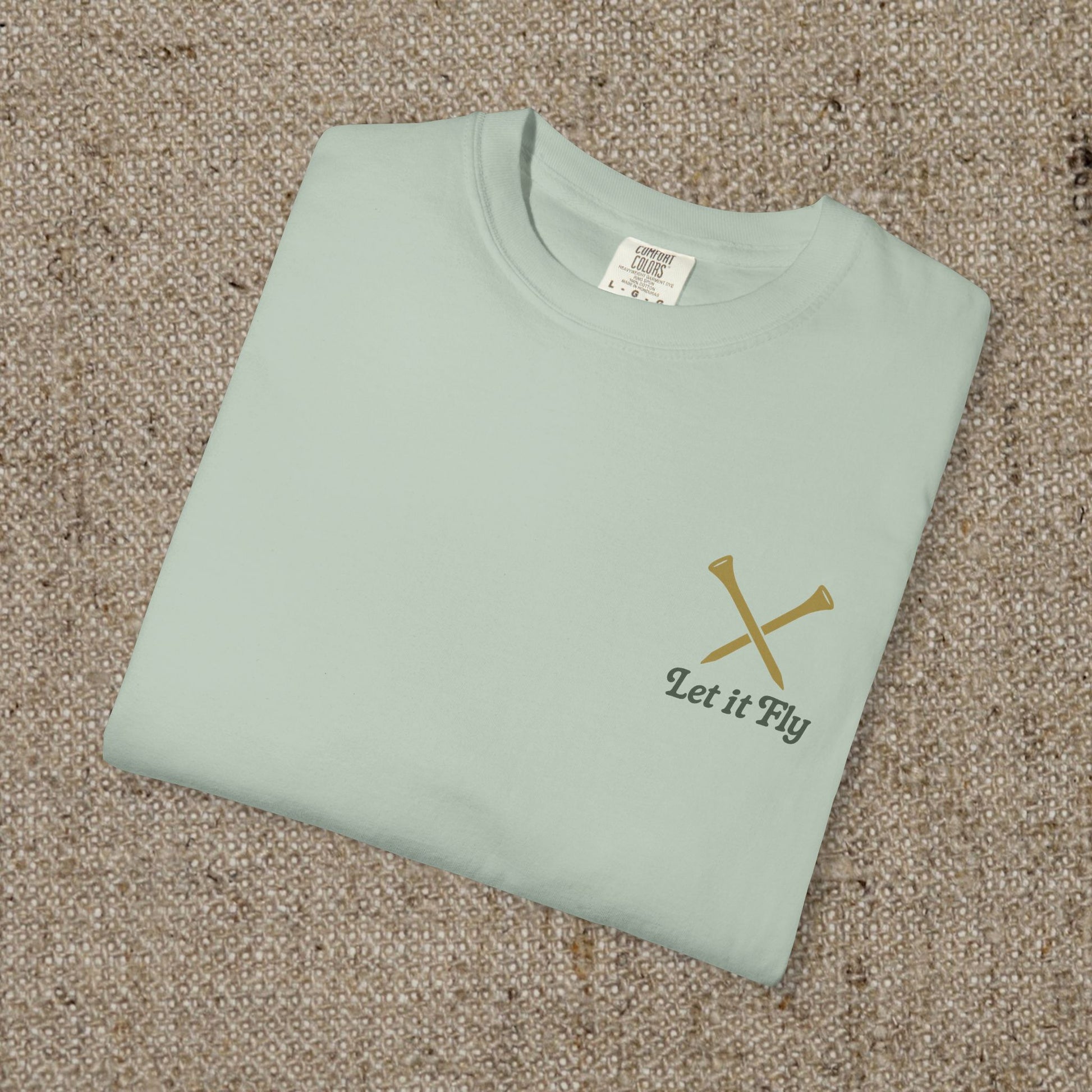 Folded Tee It High Let It Fly Graphic Tee in light green, showcasing the stylish design with 'Let It Fly' text and crossed golf clubs on the chest.