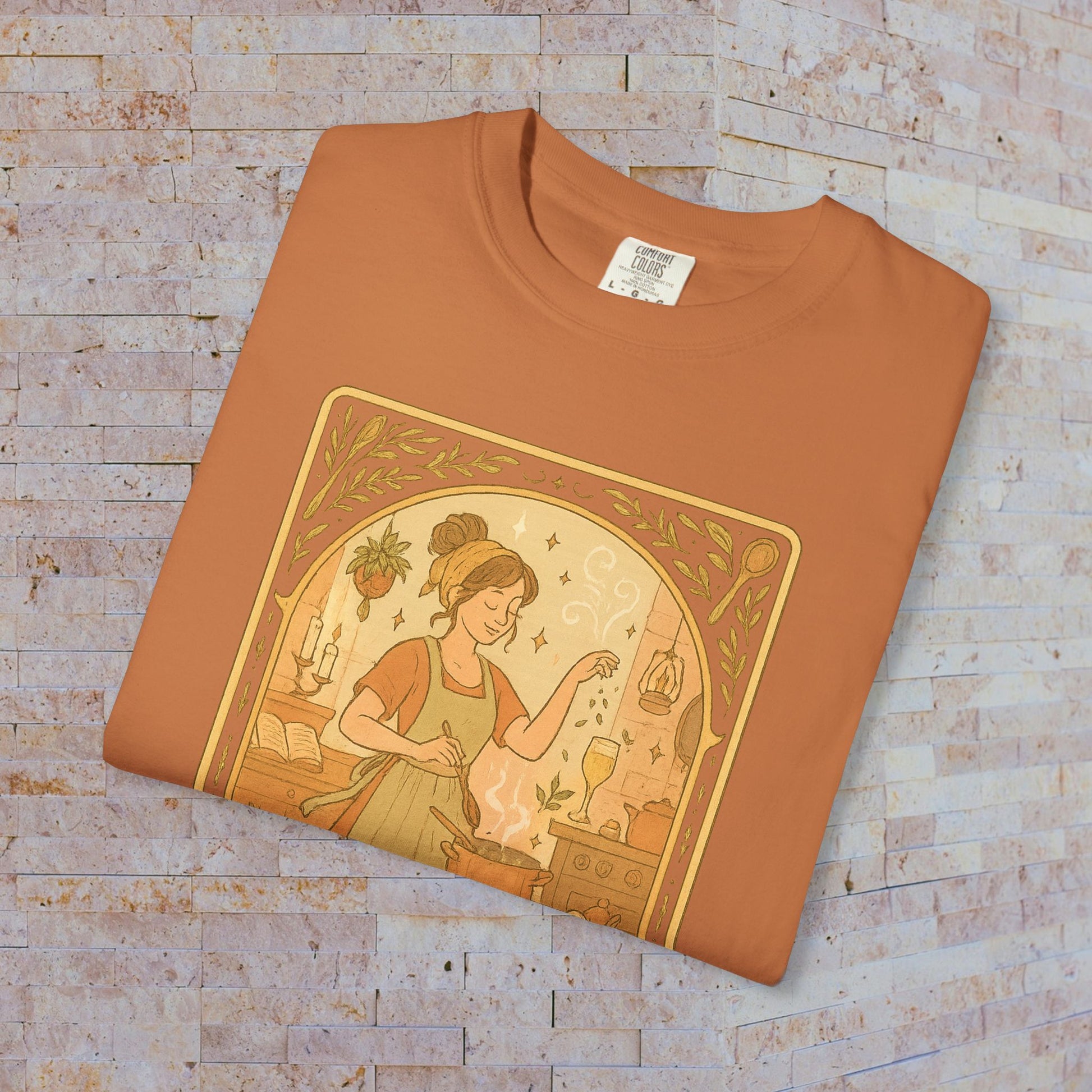 Culinary Queen Tarot Tee displayed in earthy tone, showcasing a charming illustration of a woman engaging in culinary magic. Perfect for cooking enthusiasts and tarot lovers, available in sizes S to 4XL.