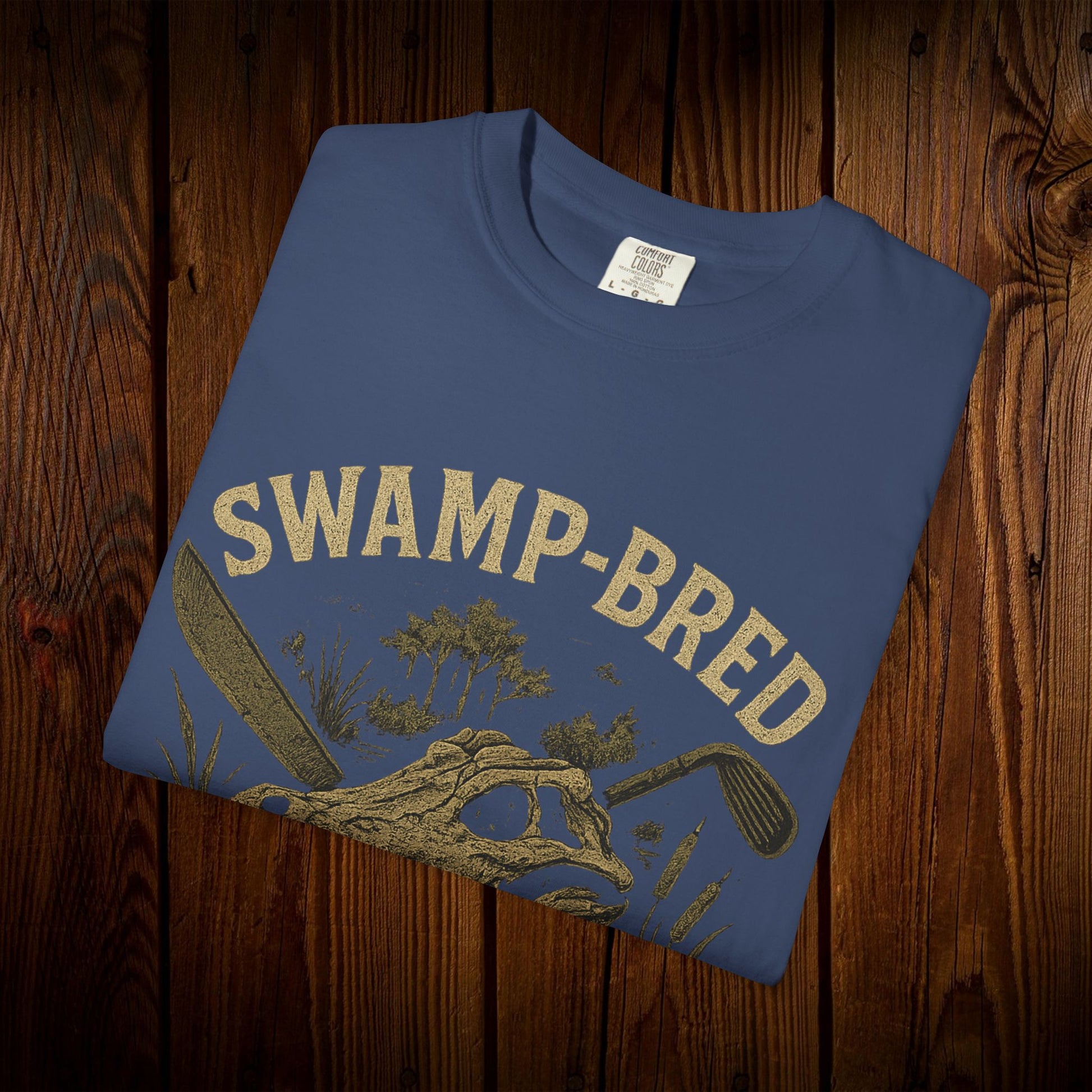 Folded Unisex Swamp-Bred Fairway-Fed Tee displaying unique graphics and high-quality fabric on wooden surface.