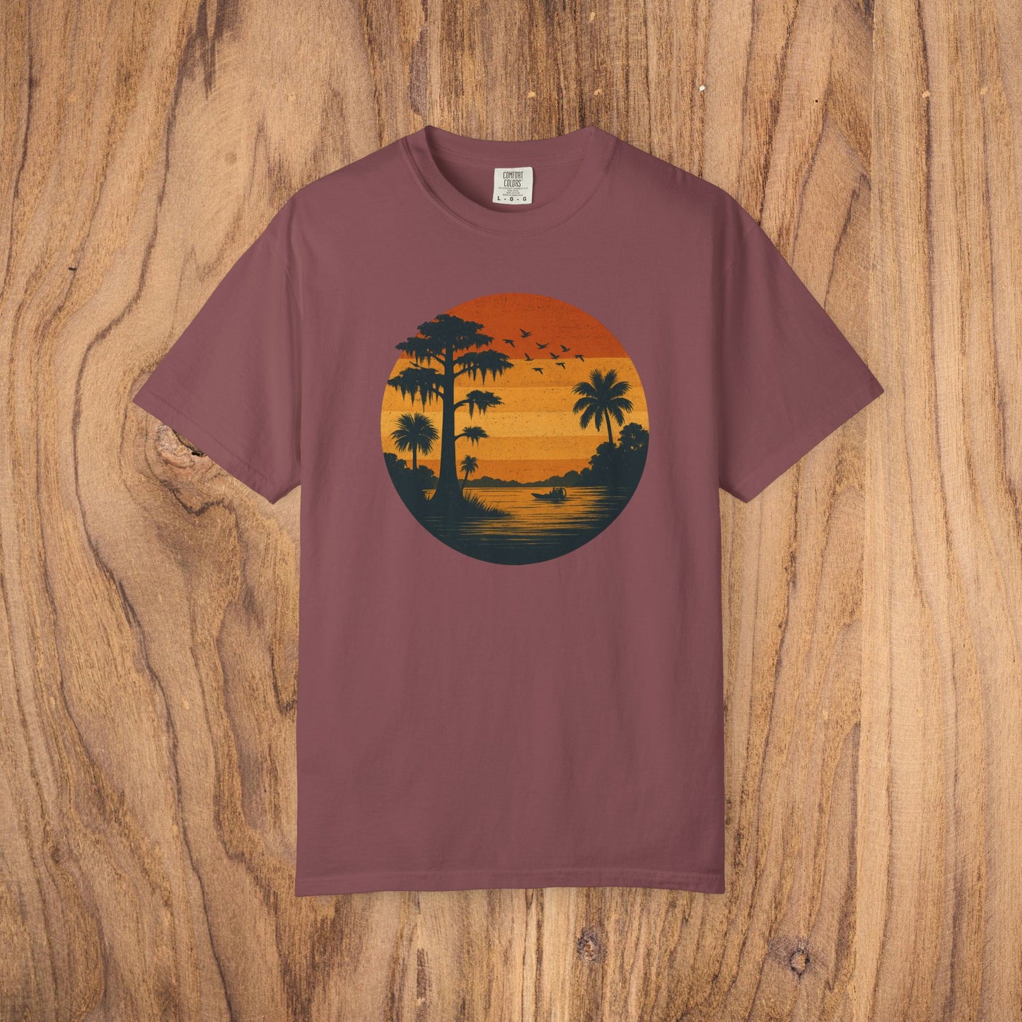 Unisex Garment-Dyed Sunset Tee in rich maroon featuring a beautiful sunset scene with palm trees and birds. Soft 100% cotton fabric available in sizes S to 4XL.