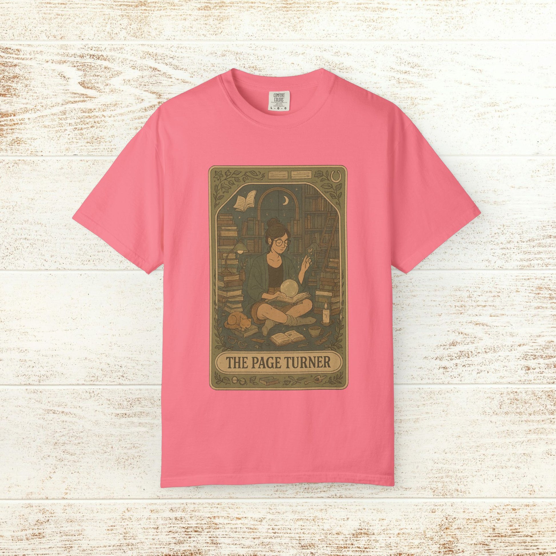 Page Turner Tarot Tee in pink, displaying a delightful graphic of a person surrounded by books in a library, crafted from soft cotton and eco-friendly materials, available in sizes S to 4XL.