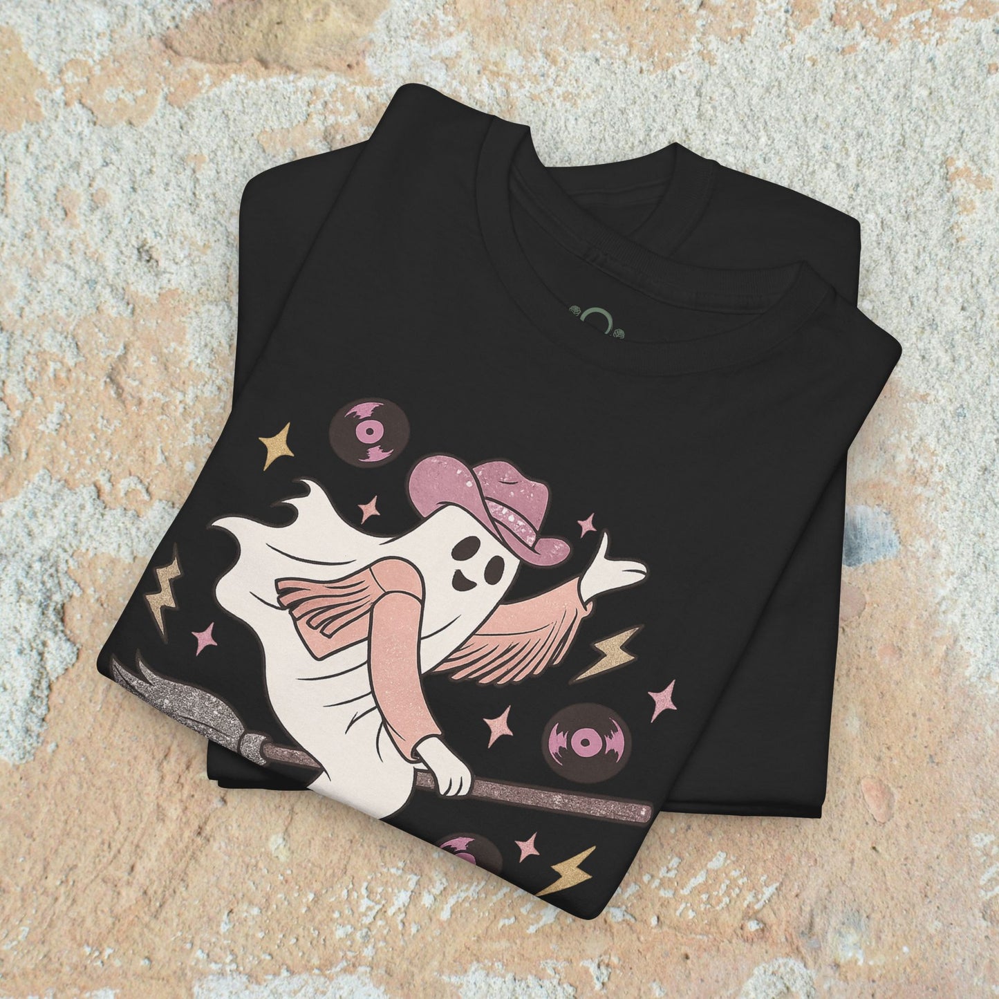 Folded Spooky Cowgirl Graphic Tee showcasing a whimsical ghost in a cowboy hat, complete with records and lightning graphics, resting on a soft fabric surface.