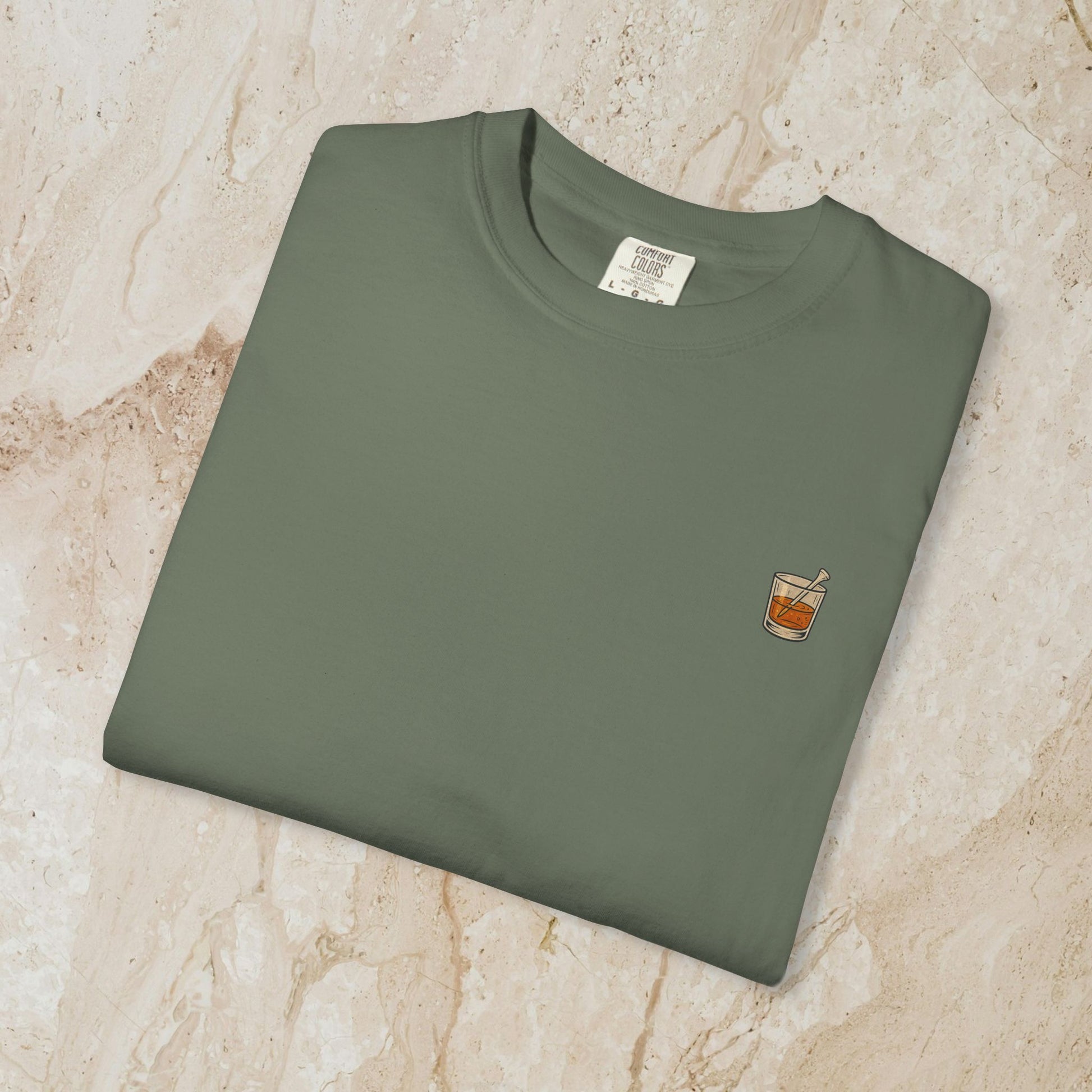 Flat lay of the Golden Whiskey Dog Tee in olive green, showcasing a casual style with a small chest pocket graphic of a drink, made from soft 100% cotton.