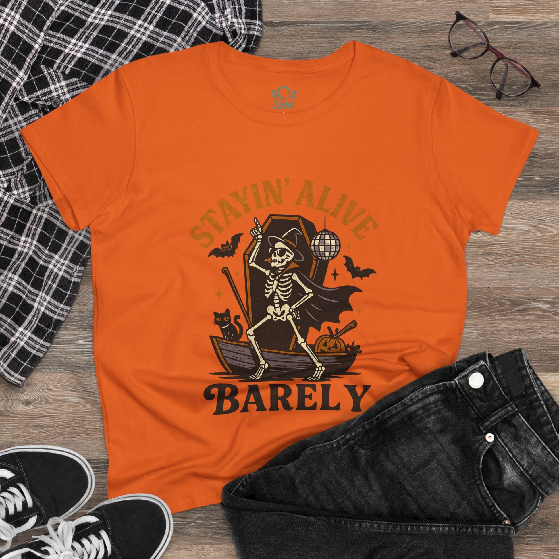 Stayin’ Alive T-Shirt in orange with a skeleton graphic, paired with stylish casual wear, perfect for Halloween and playful occasions.