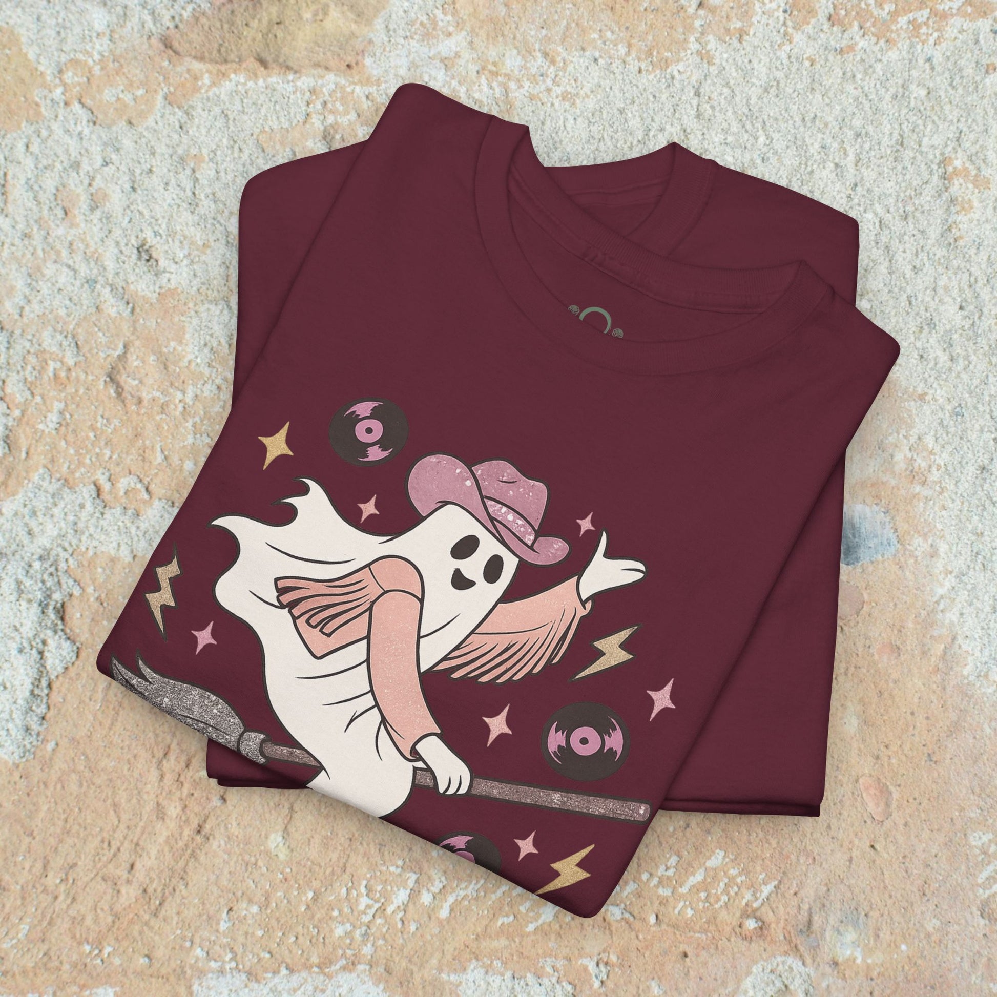 Spooky Cowgirl Graphic Tee featuring a stylish ghost character in a maroon shirt, holding a broom and wearing a cowboy hat, ideal for casual wear and available in sizes S to 5XL.