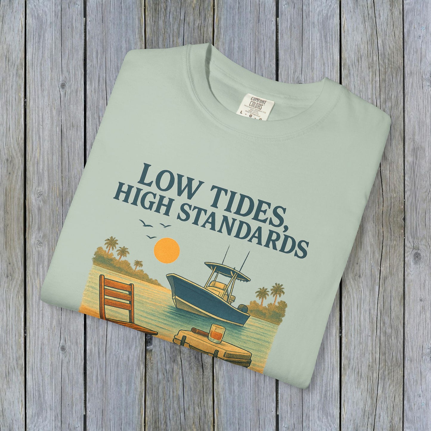 Garment-Dyed Low Tides High Standards T-Shirt laid flat on a wooden surface, emphasizing its quality fabric and vibrant print, ideal for beach lovers.