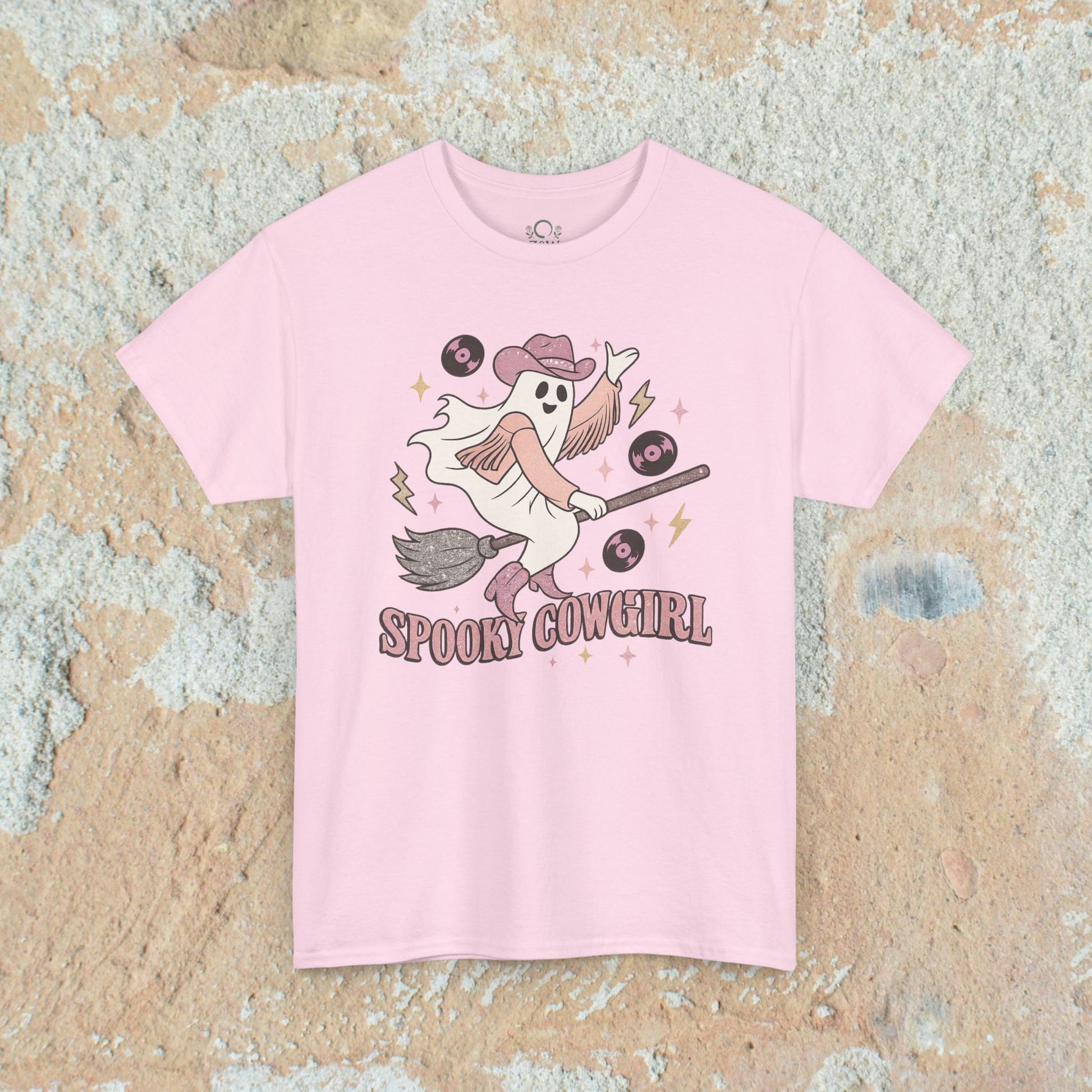Spooky Cowgirl Graphic Tee in light pink showcasing a whimsical ghostly figure with a broom, cowboy hat, and vinyl records, emphasizing comfort and available sizes from S to 5XL.