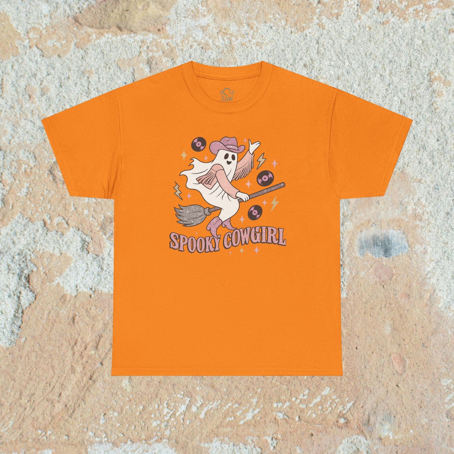 Vibrant orange Spooky Cowgirl graphic tee featuring a playful ghost with musical records and a broomstick, perfect for Halloween enthusiasts. Sizes available from S to 5XL.