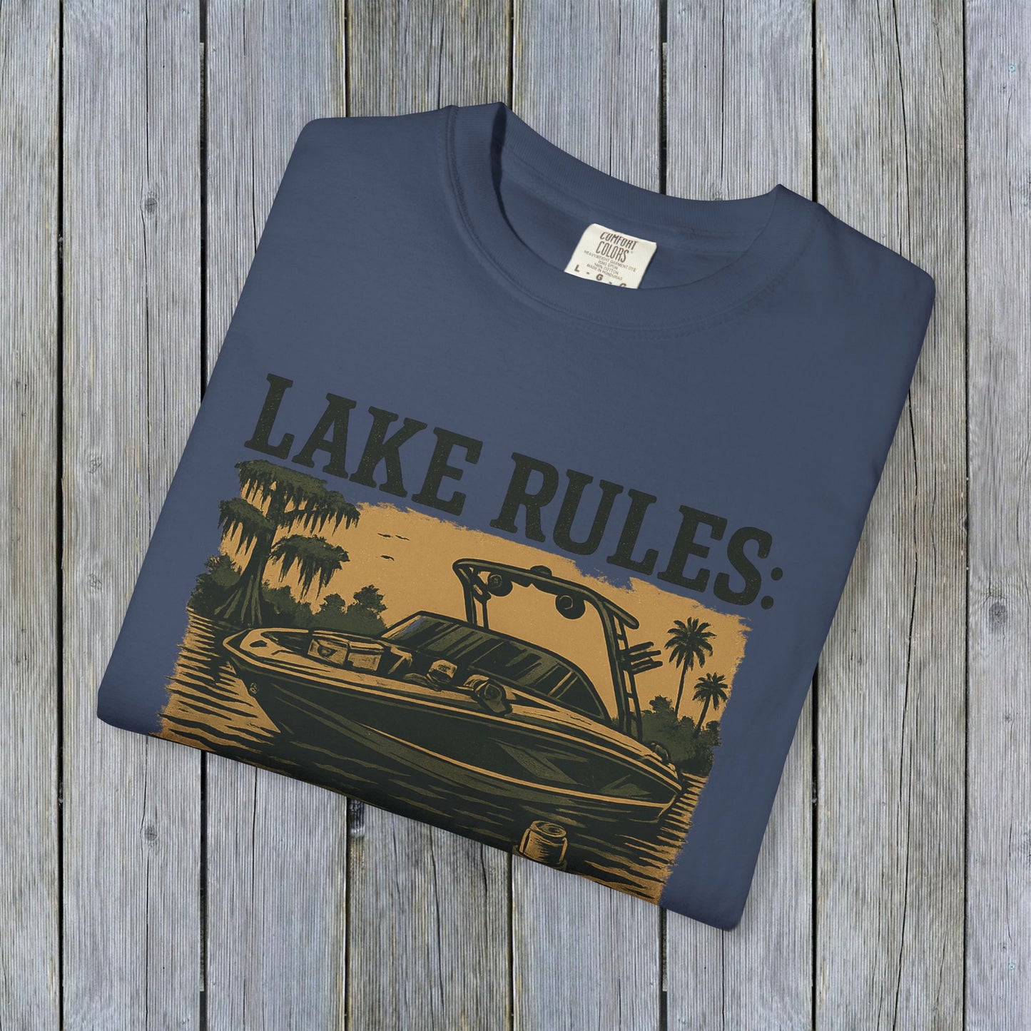 Close-up of the Unisex Garment-Dyed Lake Rules Tee - Soft Vintage Fabric, Sizes S to 4XL, featuring a vintage boat design, folded neatly on a rustic wooden surface.