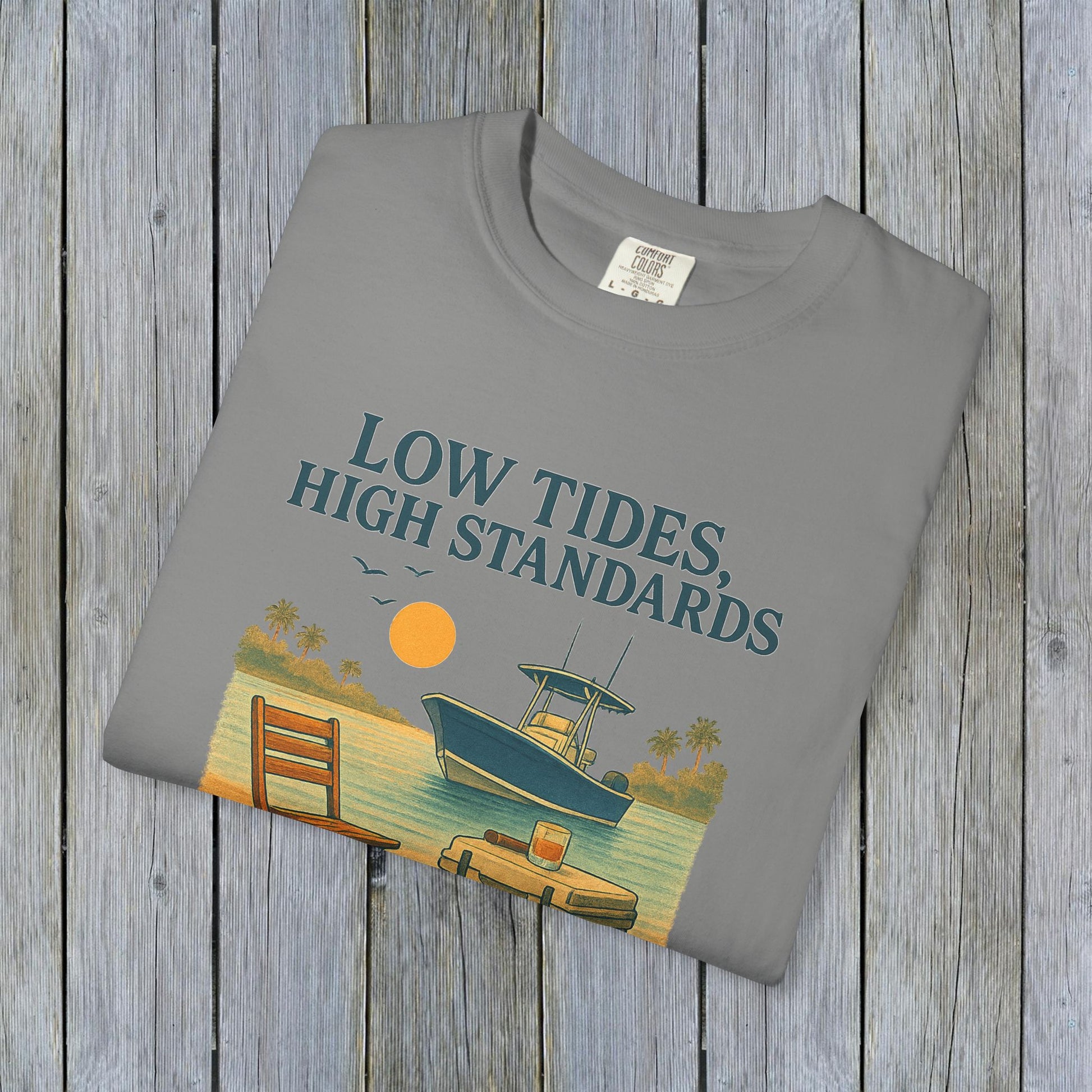 Folded Garment-Dyed Low Tides High Standards T-Shirt in gray, featuring a boat and sunny beach scene in the design. Perfect for beach outings or casual hangouts.