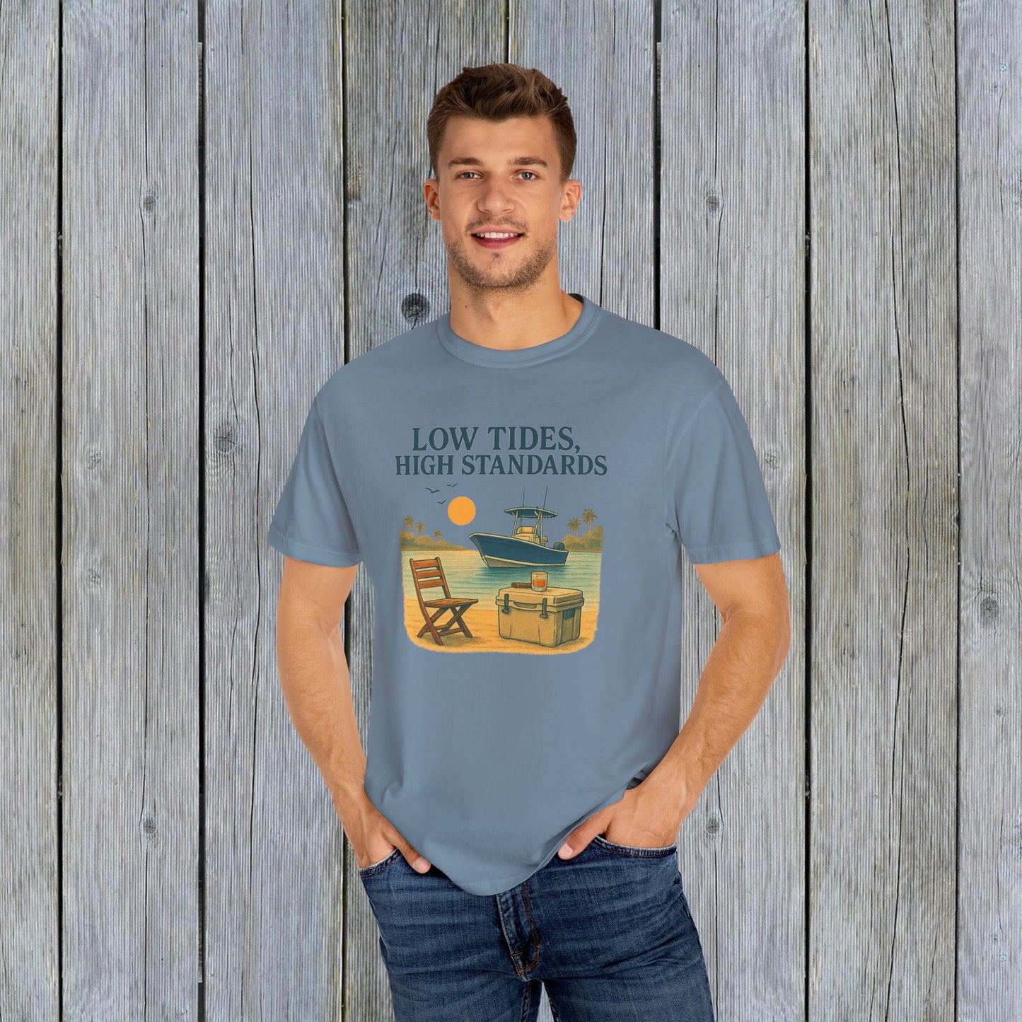 Model showcasing the Garment-Dyed Low Tides High Standards T-Shirt in light blue, ideal for casual events and beach days, with a vibrant boat graphic.