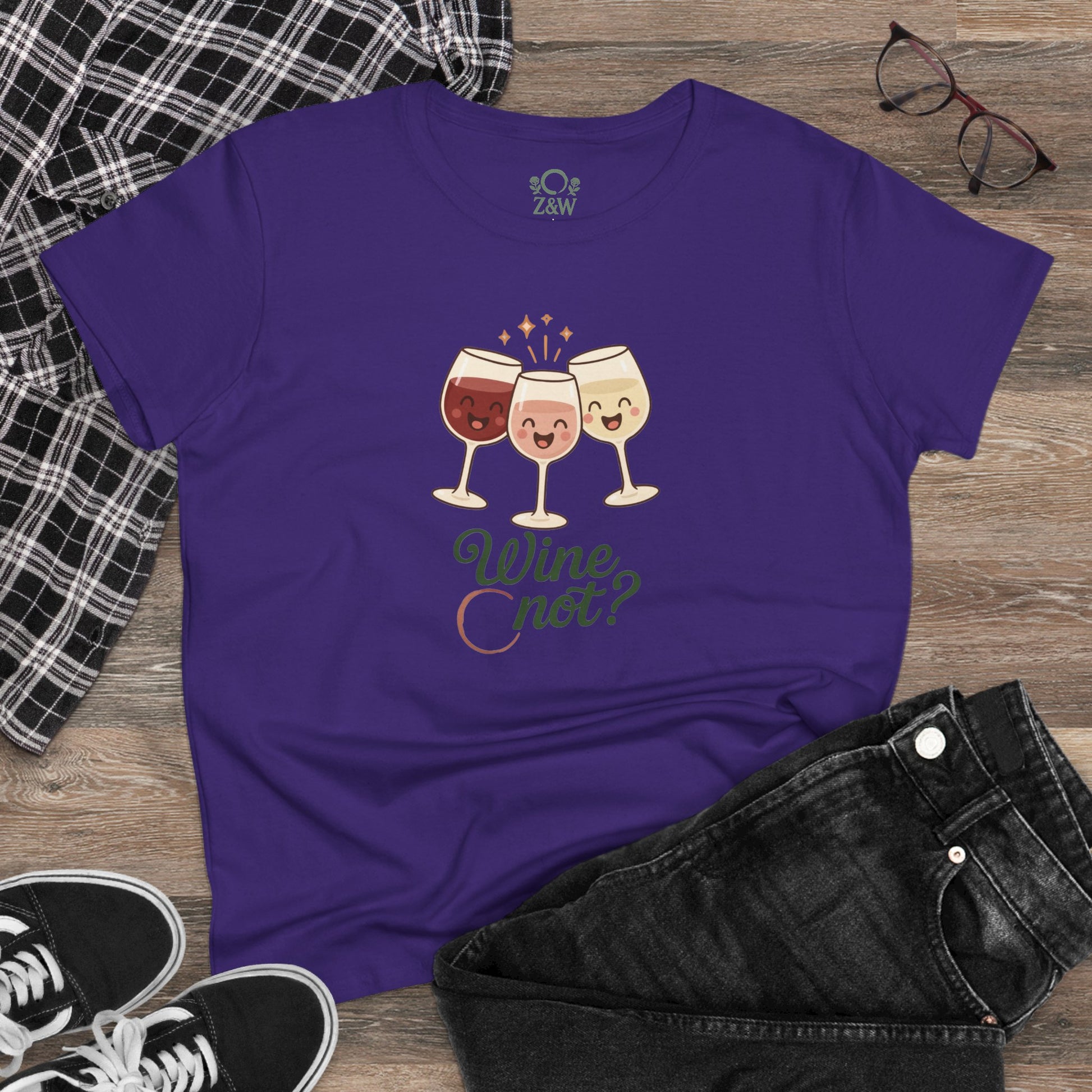 Flat lay image of the Wine Not Tee in purple with cartoon wine glasses graphic, paired with stylish black jeans, ideal for relaxed outings.
