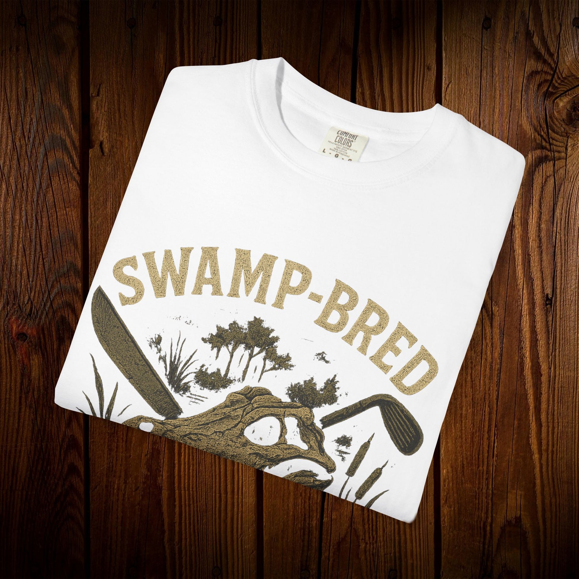 Close-up of the folded Unisex Swamp-Bred Fairway-Fed Tee in white, featuring the artistic alligator illustration, perfect for those who appreciate unique fashion.
