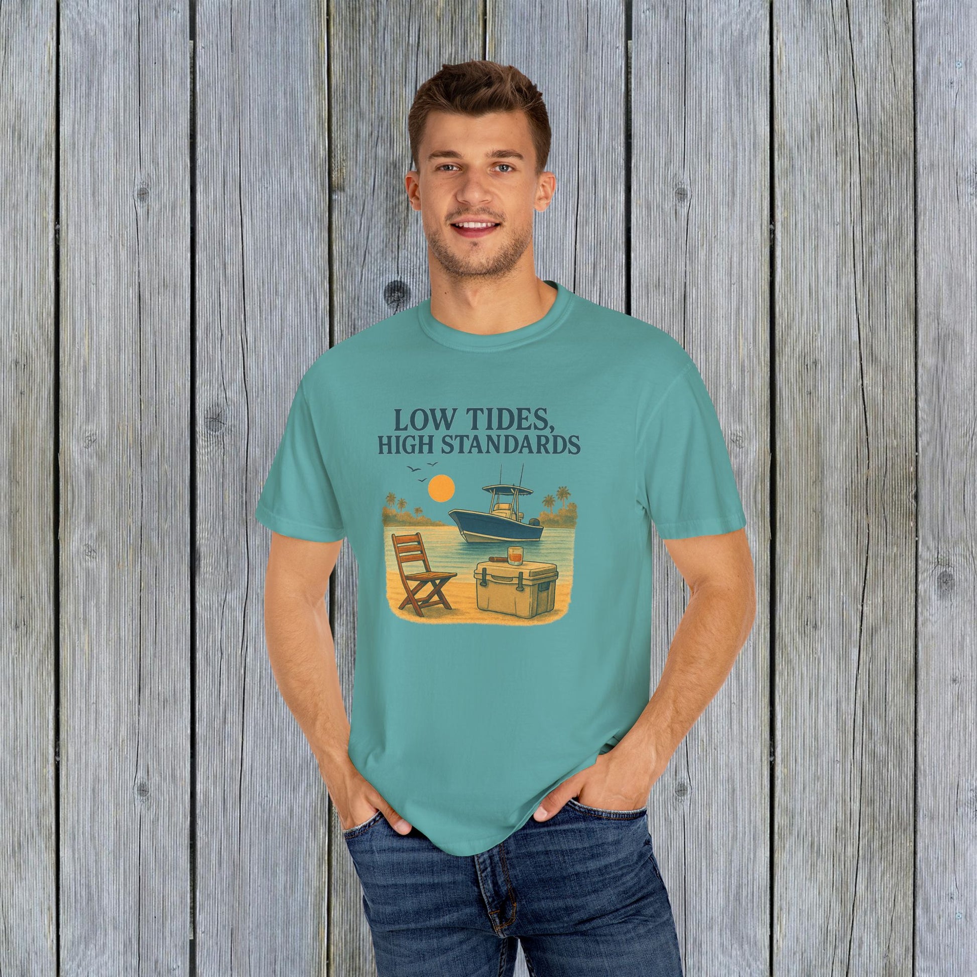 Man wearing a Garment-Dyed Low Tides High Standards T-Shirt in teal, in front of a rustic wooden backdrop, perfect for casual occasions.