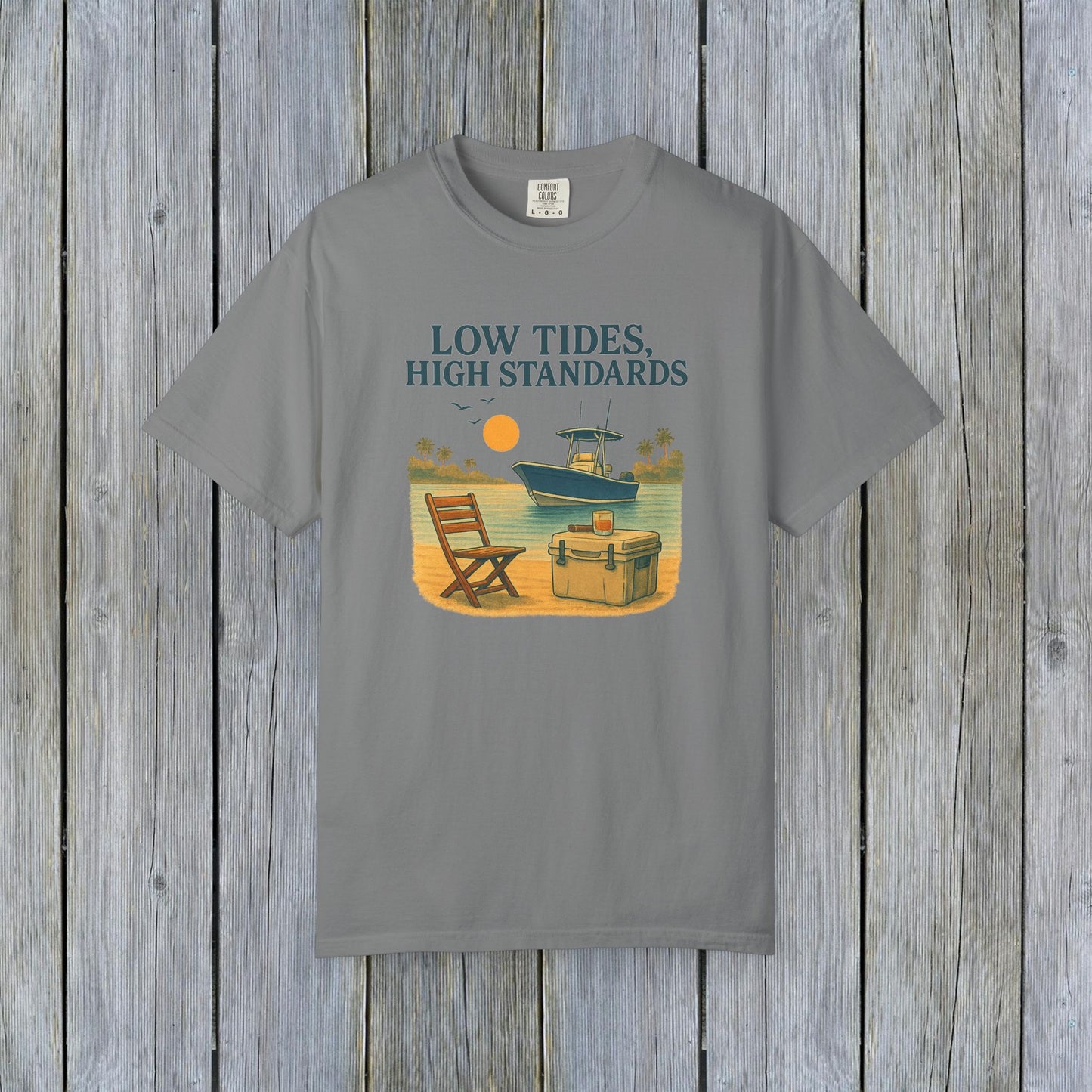 Garment-Dyed Low Tides High Standards T-Shirt in gray, illustrating a laid-back beach scene with a chair and boat. Made from soft 100% US cotton, this shirt is available in sizes S-4XL.