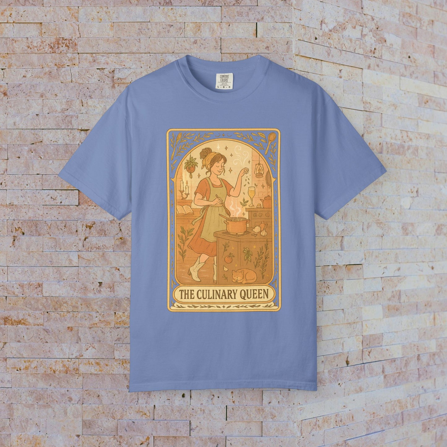 Culinary Queen Tarot Tee in blue, presenting a whimsical illustration of a girl baking. This tee is crafted from soft, pre-shrunk cotton and is available in sizes S to 4XL.