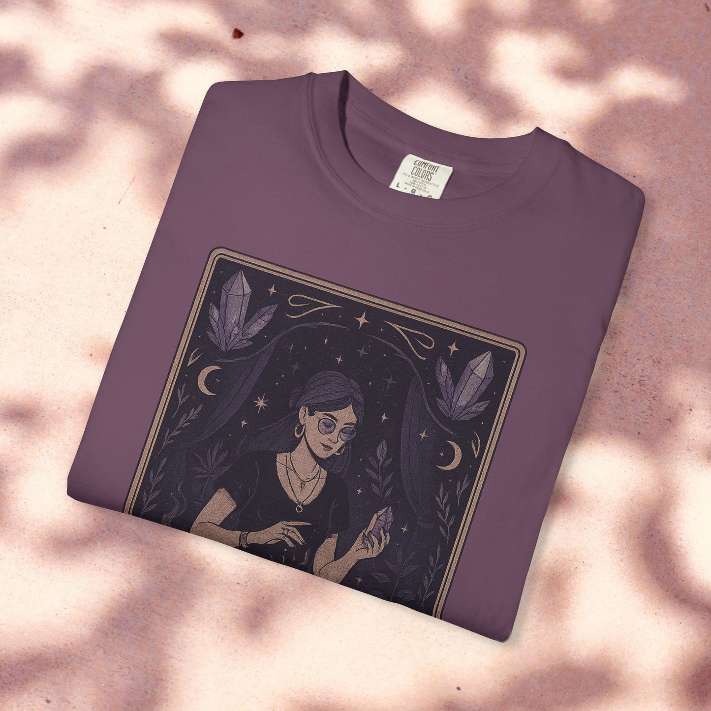 Intuitive Tarot Tee in a rich purple hue, presented on a light pink background, featuring a serene woman and mystical crystals, made from soft 100% cotton.