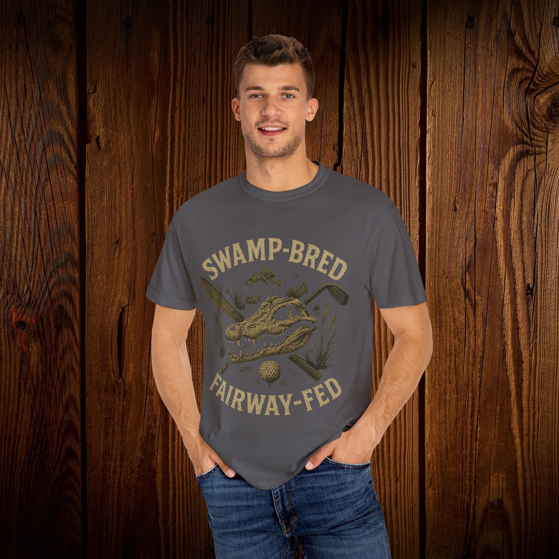 Model wearing the Unisex Swamp-Bred Fairway-Fed Tee in a neutral tone, standing against a rustic wooden backdrop. The tee features a stylish design ideal for golf enthusiasts, available in sizes S to 4XL.