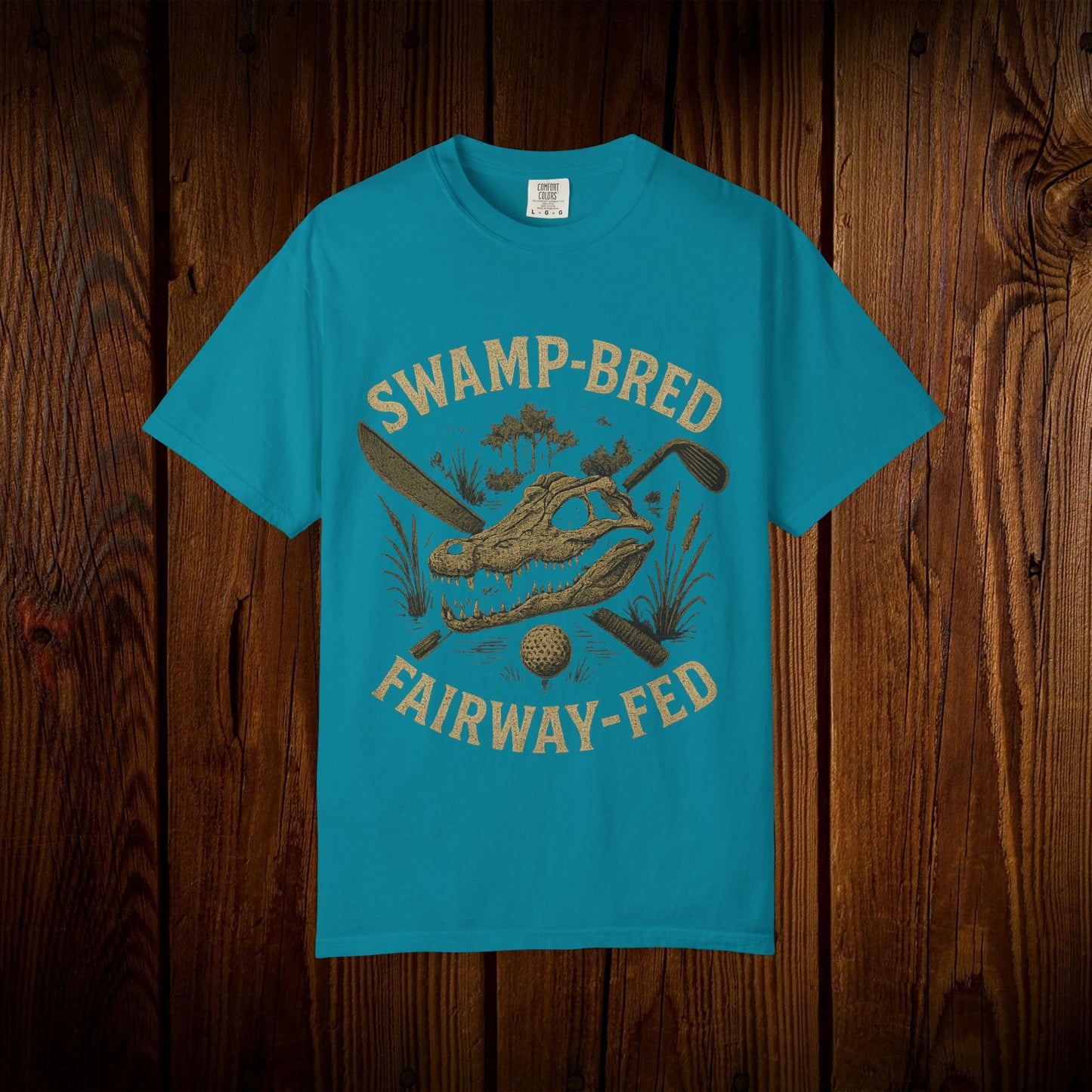 Unisex Swamp-Bred Fairway-Fed Tee in bright turquoise, displaying a bold graphic of an alligator skull crossed with golf clubs, complemented by a textured wood background.