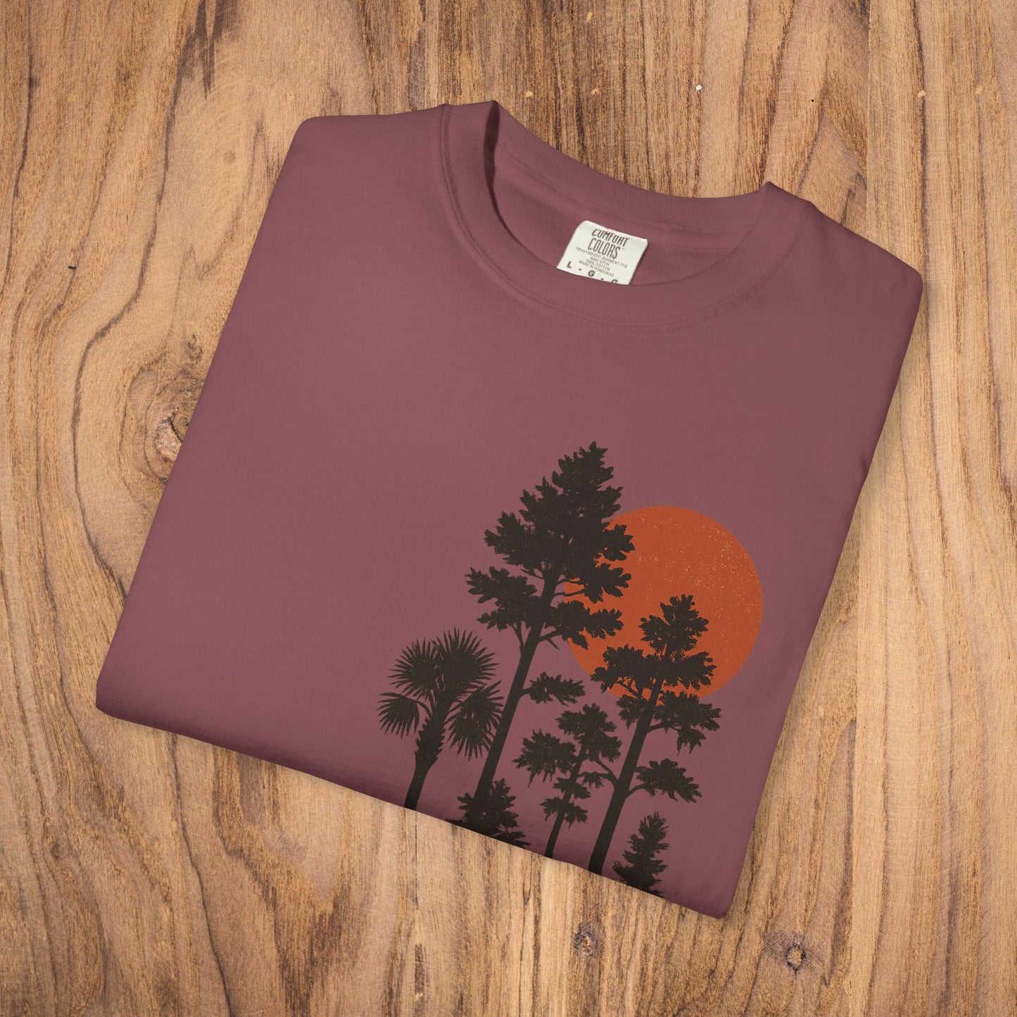 Front laid flat view of the Sunset Trees Unisex T-Shirt in burgundy, featuring a beautiful tree silhouette against a vibrant sunset, made from quality 100% cotton.