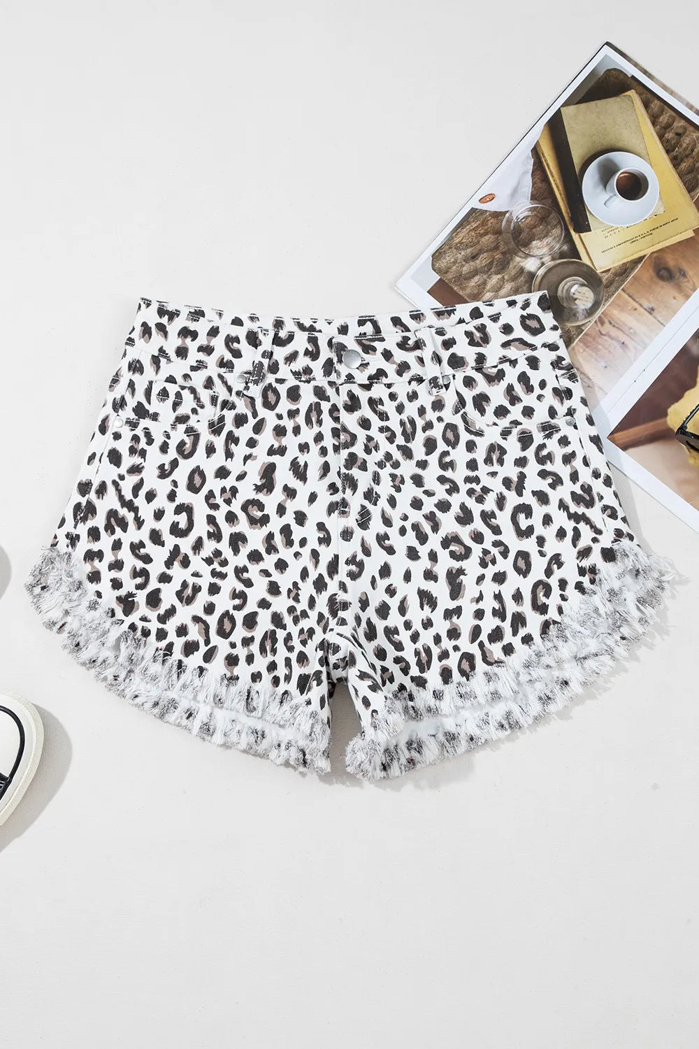 Flat lay of leopard frayed hem denim shorts on a neutral background, featuring a chic and fashionable pattern ideal for summer wardrobes.