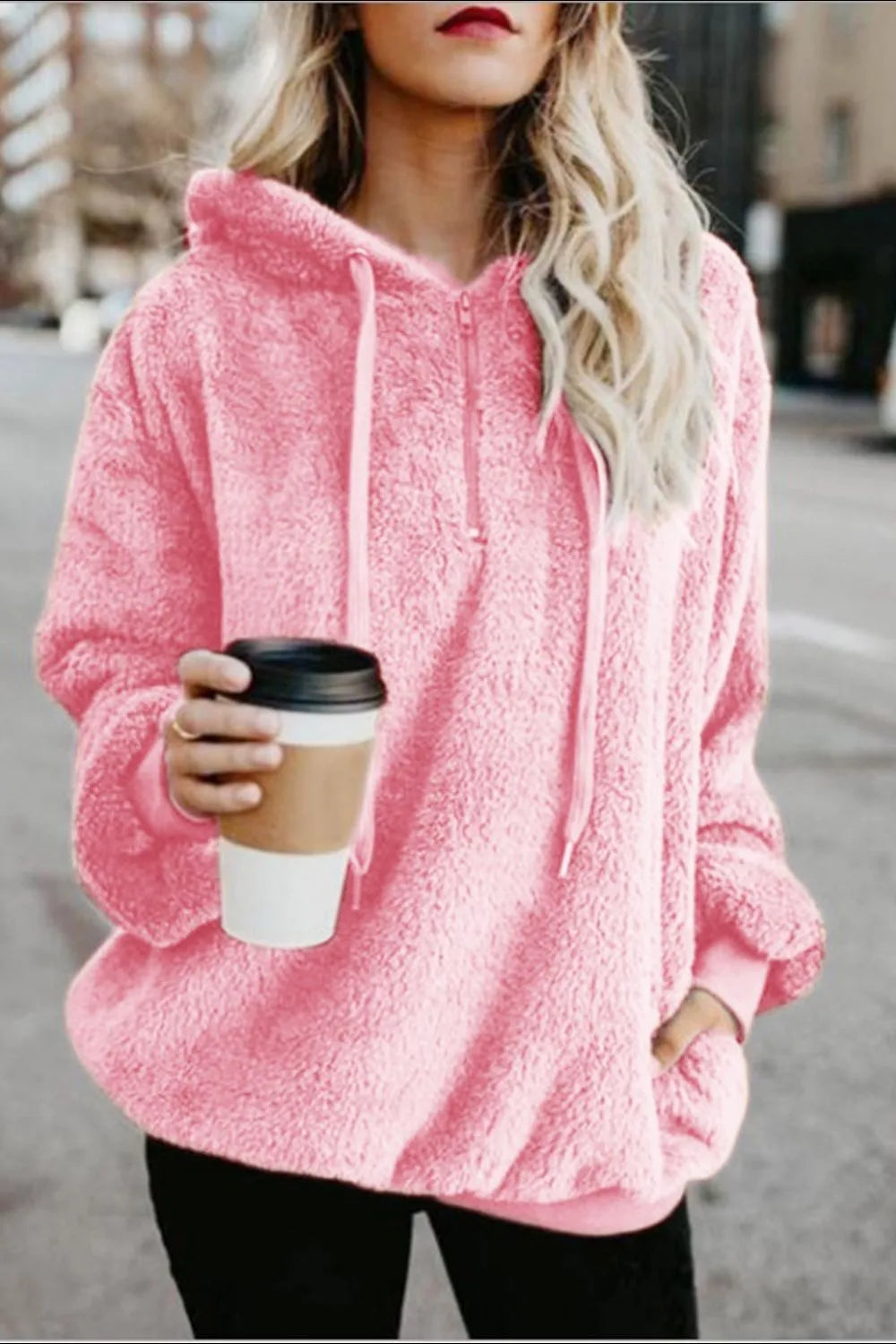 Model sporting a Cozy Full Size Teddy Hoodie with Quarter-Zip and Drawstring in pink, enjoying a coffee in an urban setting.
