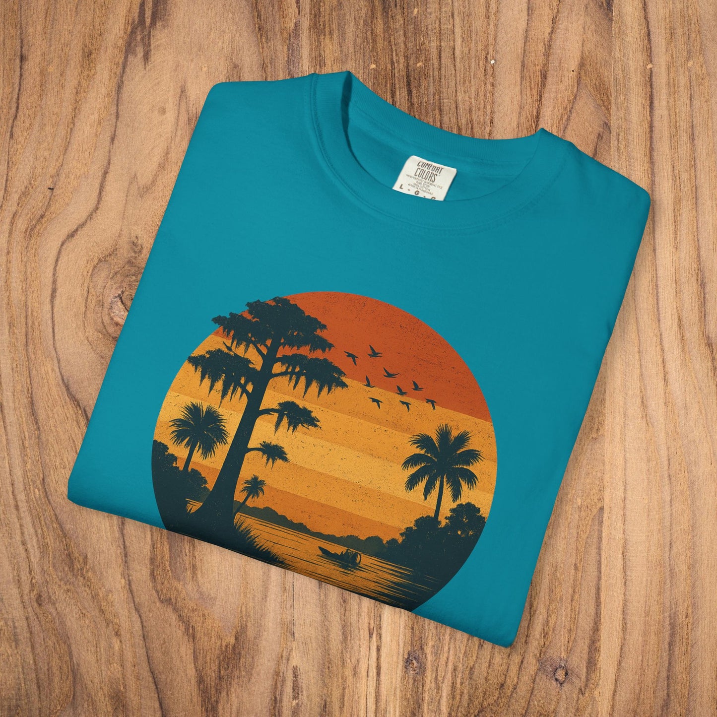 Unisex Garment-Dyed Sunset Tee in a vibrant teal color with a graphic of a sunset and palm trees, made from 100% cotton for a relaxed fit.