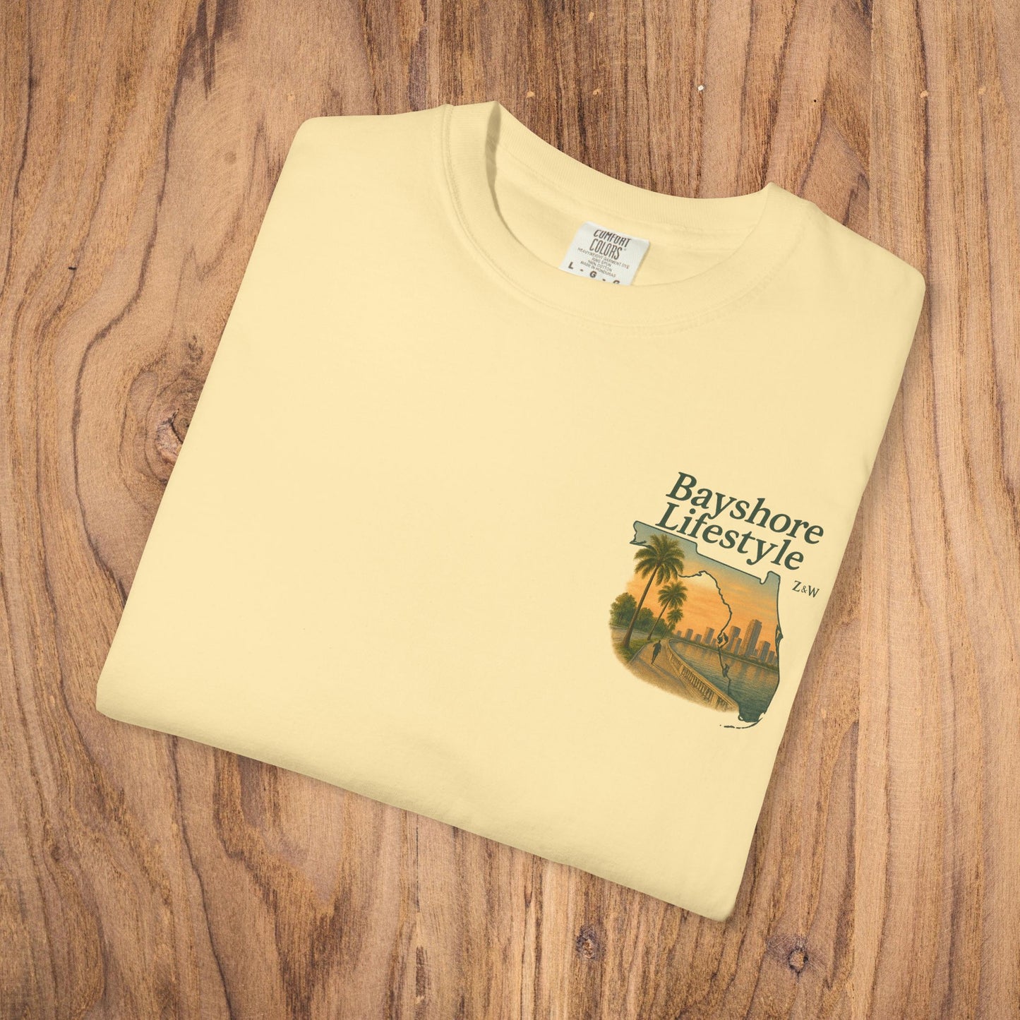 Bayshore Lifestyle Tee - Folded yellow t-shirt featuring a graphic design, laid out on a wooden surface.