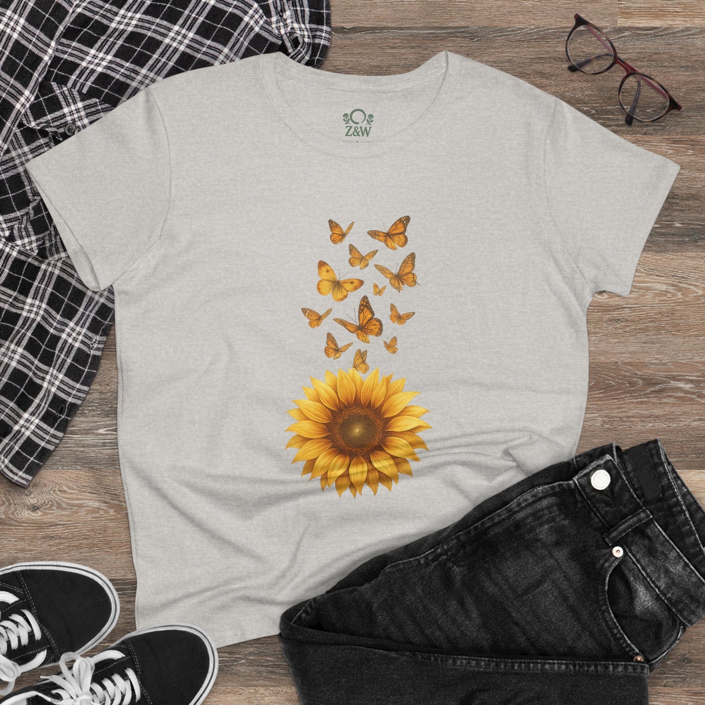 Sunflower & Butterflies Cotton Tee for Women displayed on a wooden surface, featuring a vibrant sunflower graphic with butterflies, showcasing 100% soft cotton, breathable and durable design.
