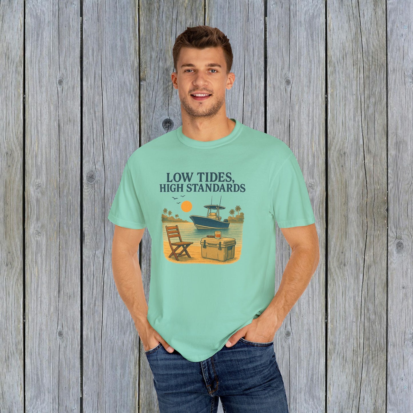 Man wearing the Garment-Dyed Low Tides High Standards T-Shirt in mint green, with a cheerful beach graphic. Great for a relaxed summer look.