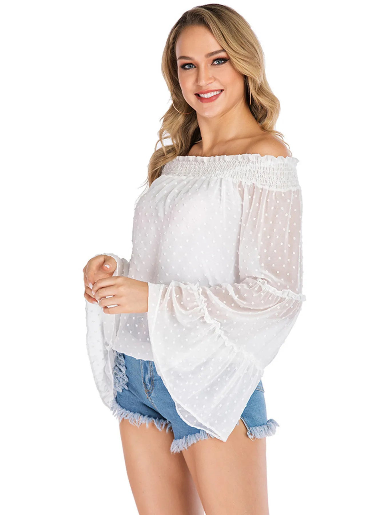 Model wearing the Trendsi Swiss Dot Off-Shoulder Blouse in white, featuring tiered frill and sheer fabric, styled with denim shorts, ideal for a casual chic look.
