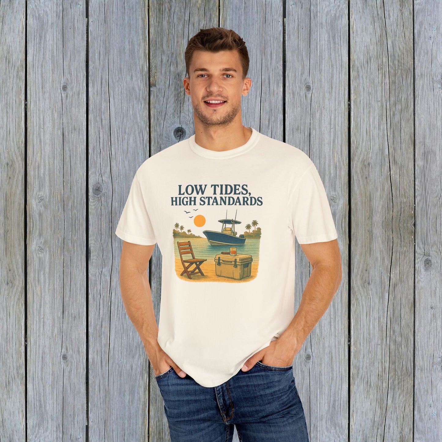 Man modeling Garment-Dyed Low Tides High Standards T-Shirt in cream, showcasing a laid-back lifestyle with a boat and sunset backdrop.