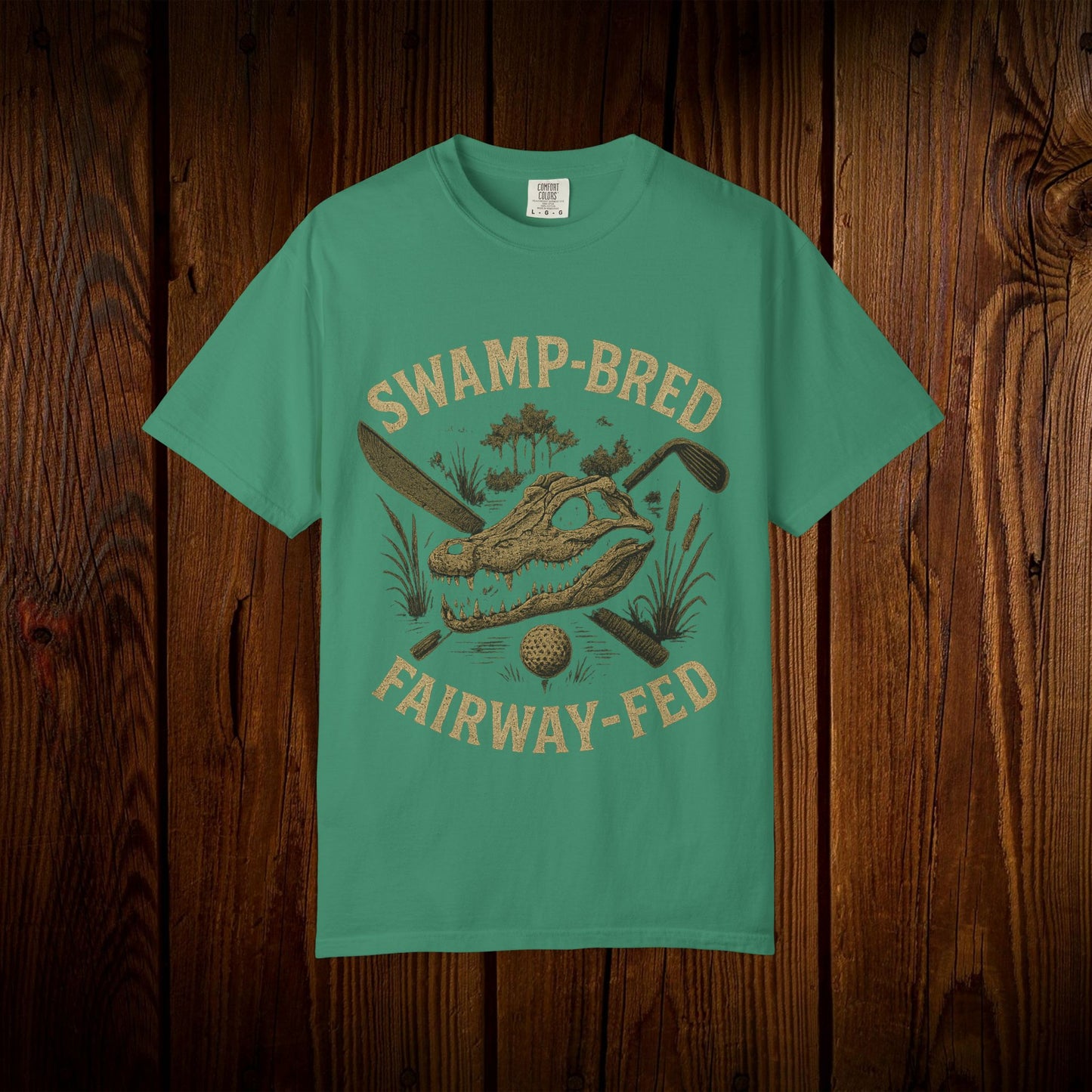 Unisex Swamp-Bred Fairway-Fed Tee in vibrant teal, featuring a distinctive graphic of an alligator skull and golf clubs, set against a wooden backdrop.