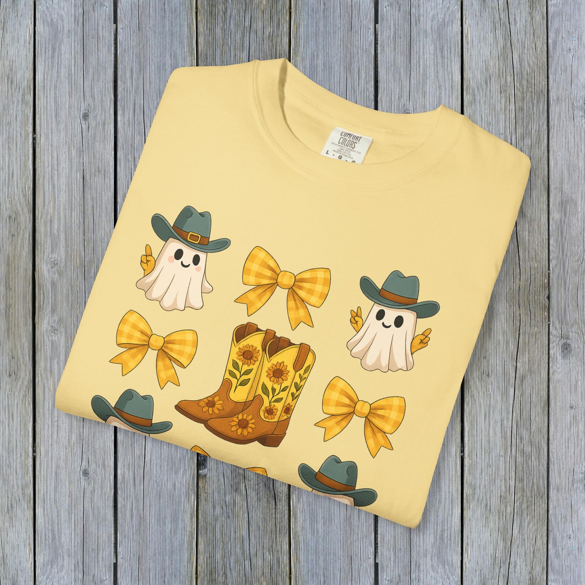 Cute Halloween T-Shirt design featuring cheerful ghosts, cowboy boots, and yellow bows, neatly folded and displayed against a weathered wooden surface, perfect for stylish eco-friendly attire.
