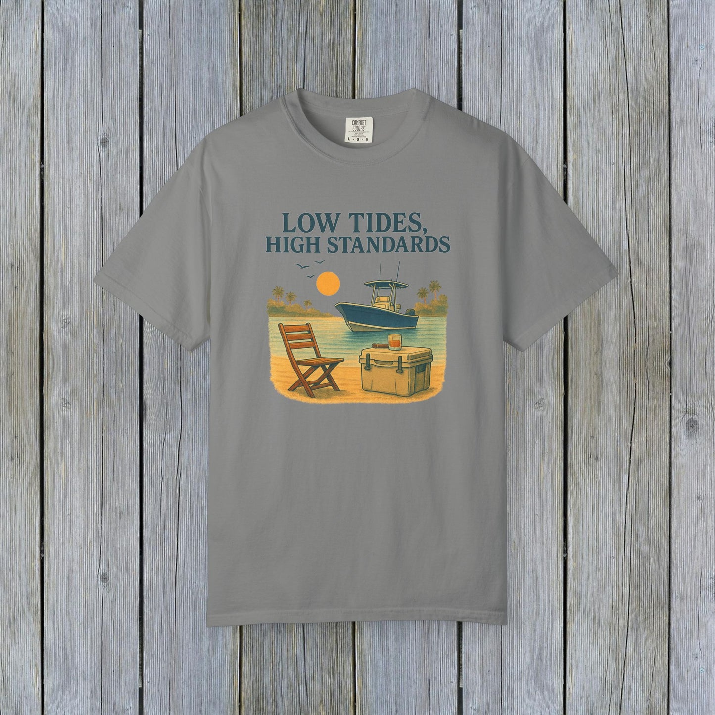 Garment-Dyed Low Tides High Standards T-Shirt in grey color, displaying an idyllic beach scene with a chair, cooler, and boat. This shirt is made from soft 100% US cotton and comes in sizes S-4XL.